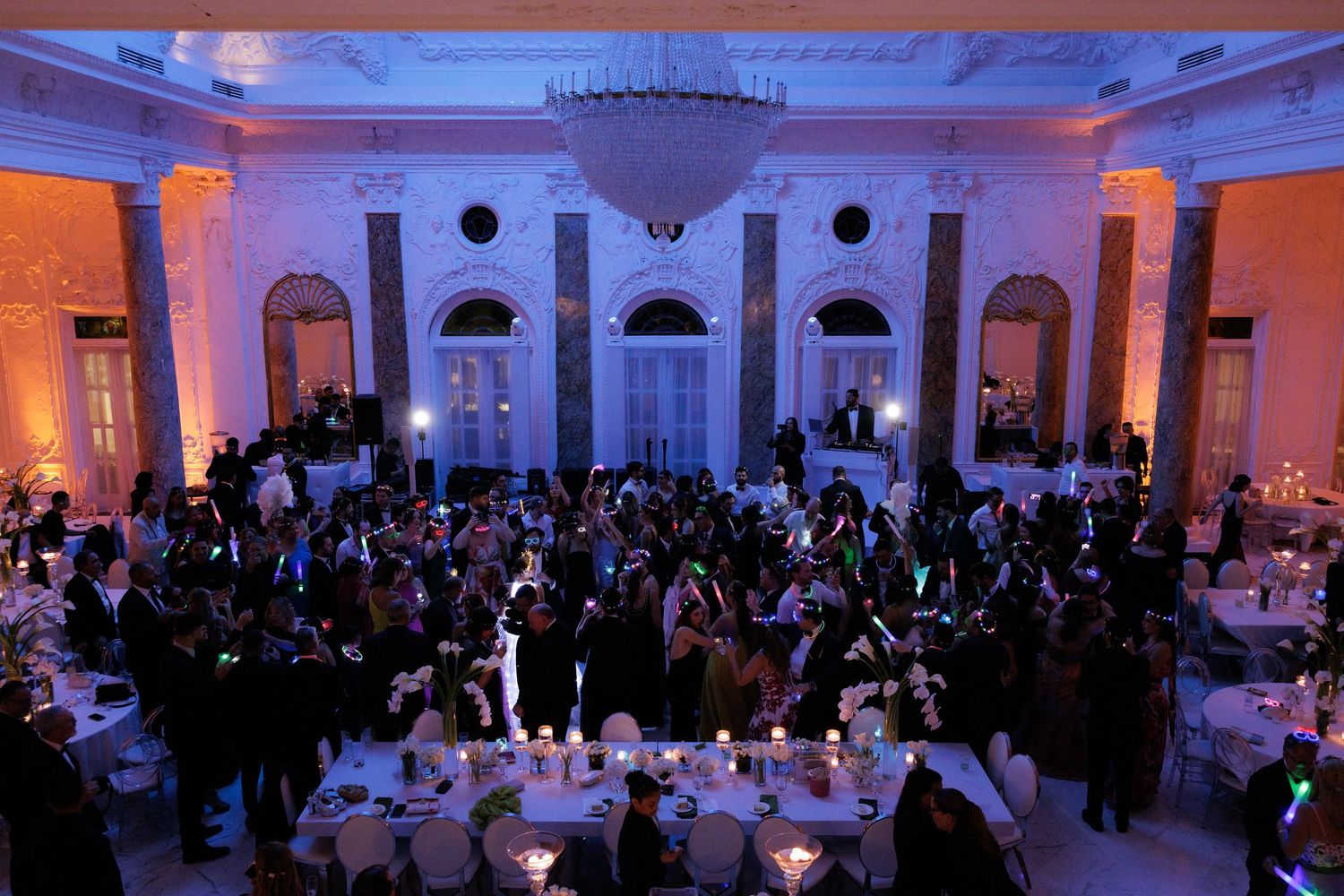 Large ballroom event space illuminated in blue and orange lighting with guests mingling during an elegant reception.