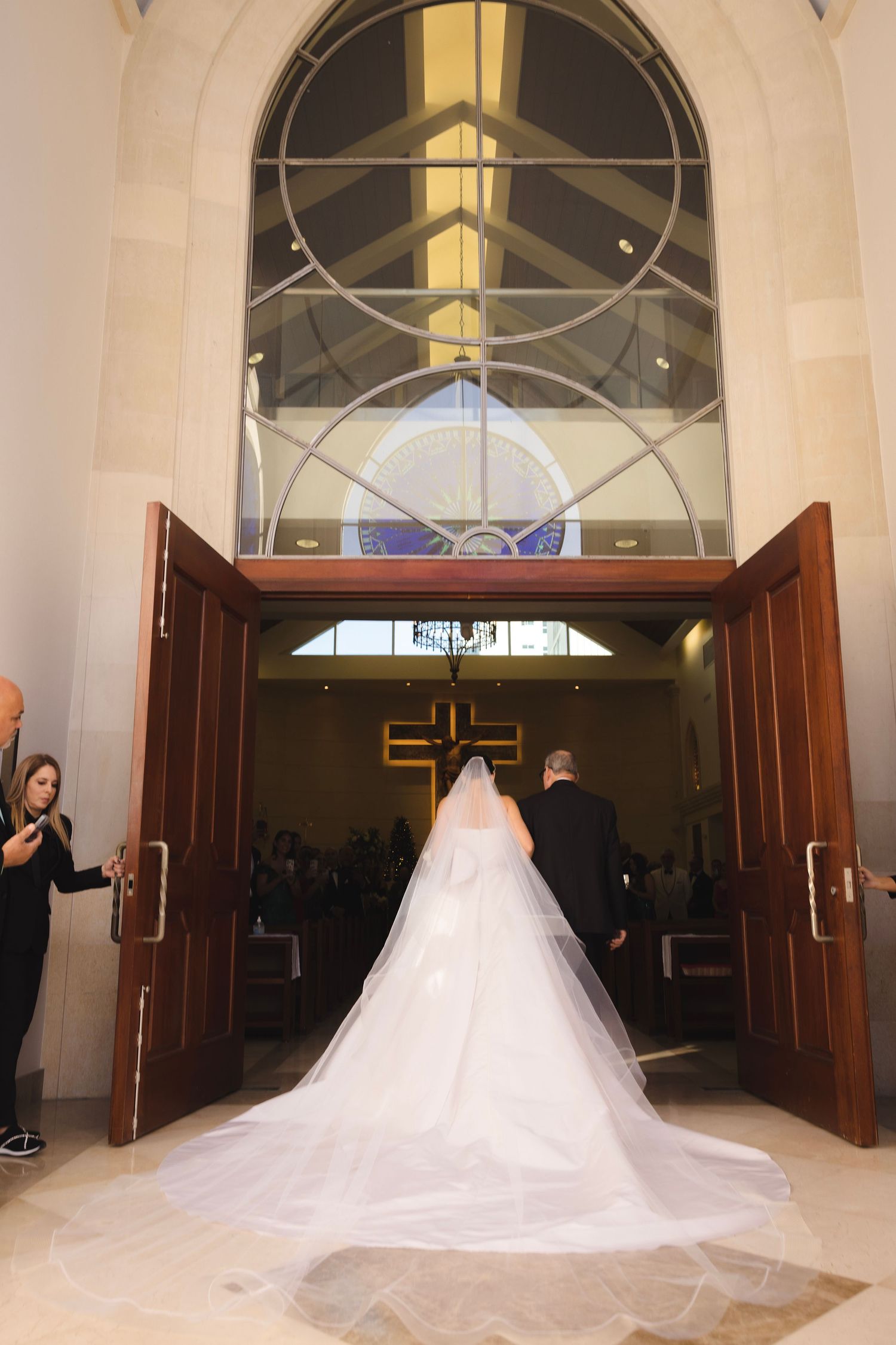 A stunning cathedral wedding with a grand entrance and dramatic train of a white wedding gown flowing through the doorway.