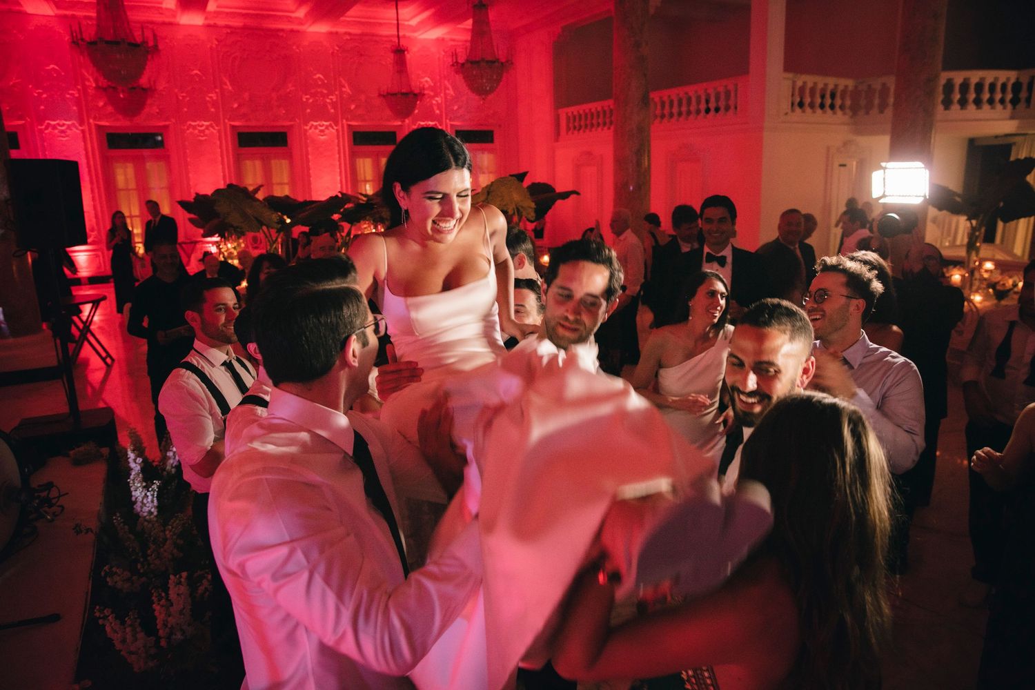 Wedding reception dance party with vibrant red lighting fills an elegant ballroom with celebrating guests.