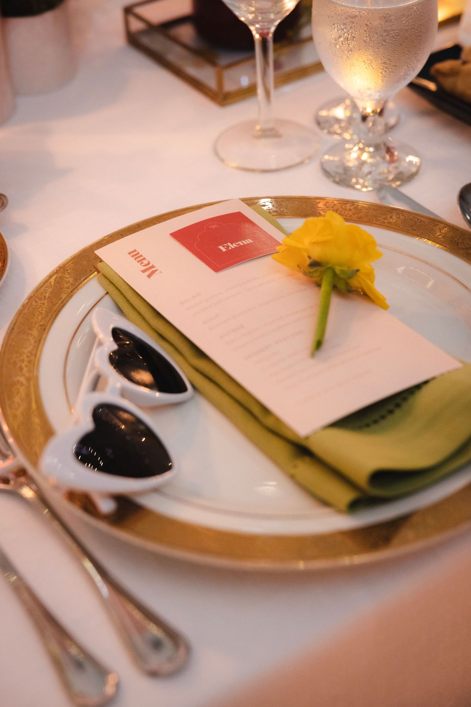 Elegant restaurant table settings with menus, shades of green napkins, and gold-rimmed plates on white tablecloths.