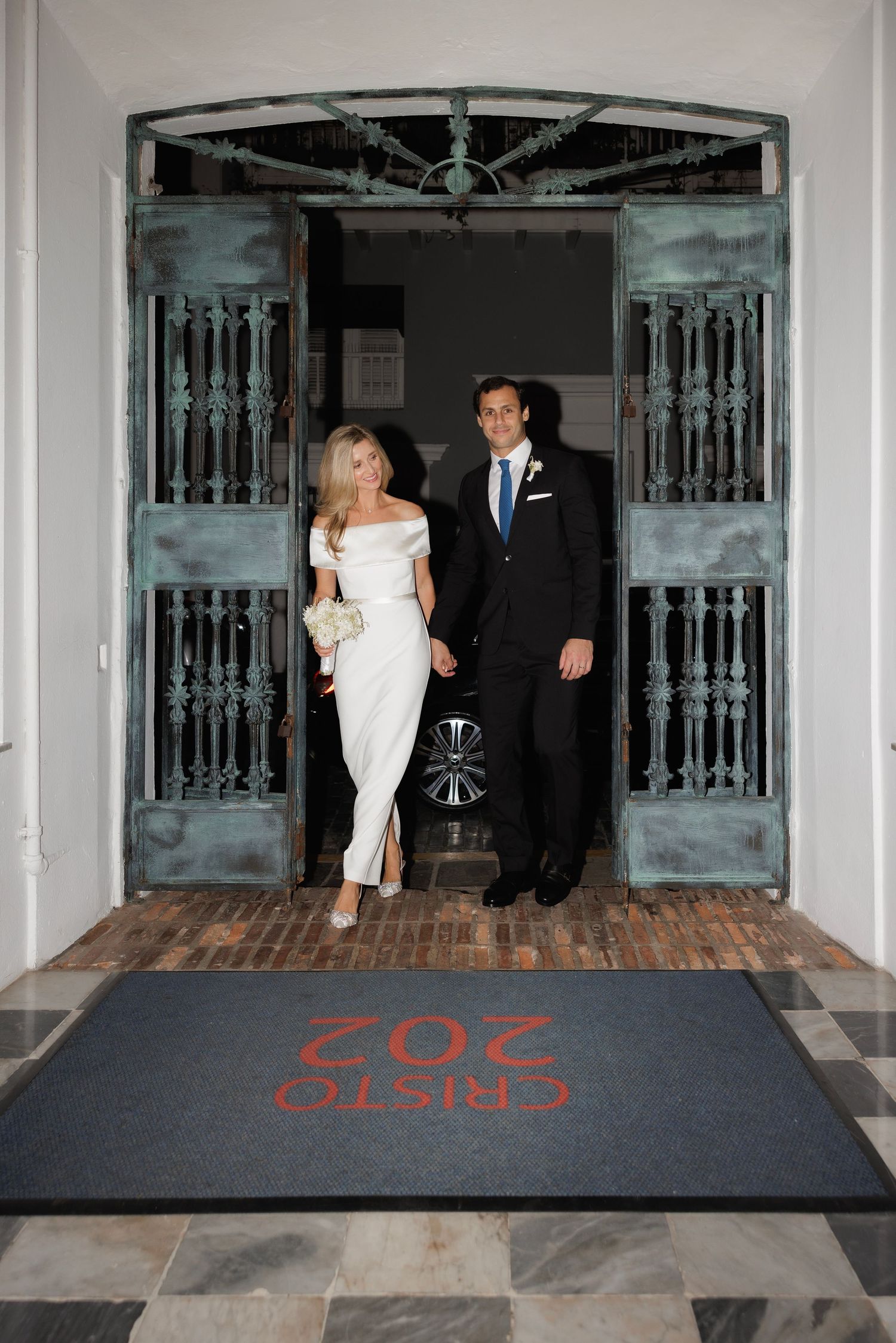 Four progressive wedding photos show a couple walking down a vintage hallway with ornate railings and a luxury carpet.