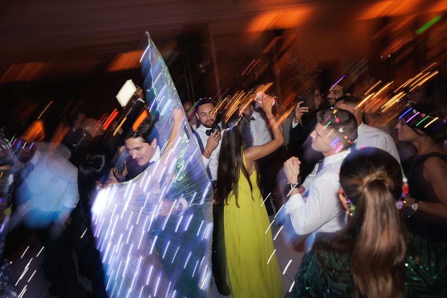 Dynamic dance party scene with motion blur capturing energetic movement under dramatic orange lighting.