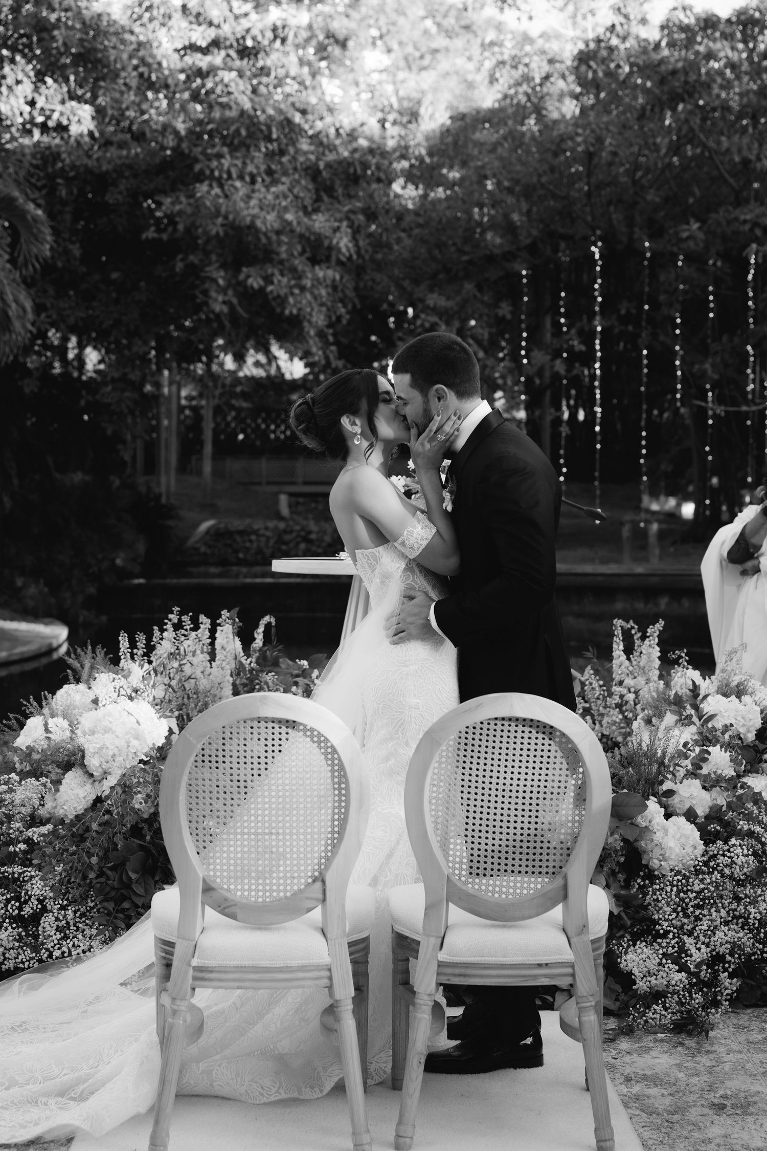 Romantic evening wedding reception with vintage white chairs and twinkling lights in garden setting.