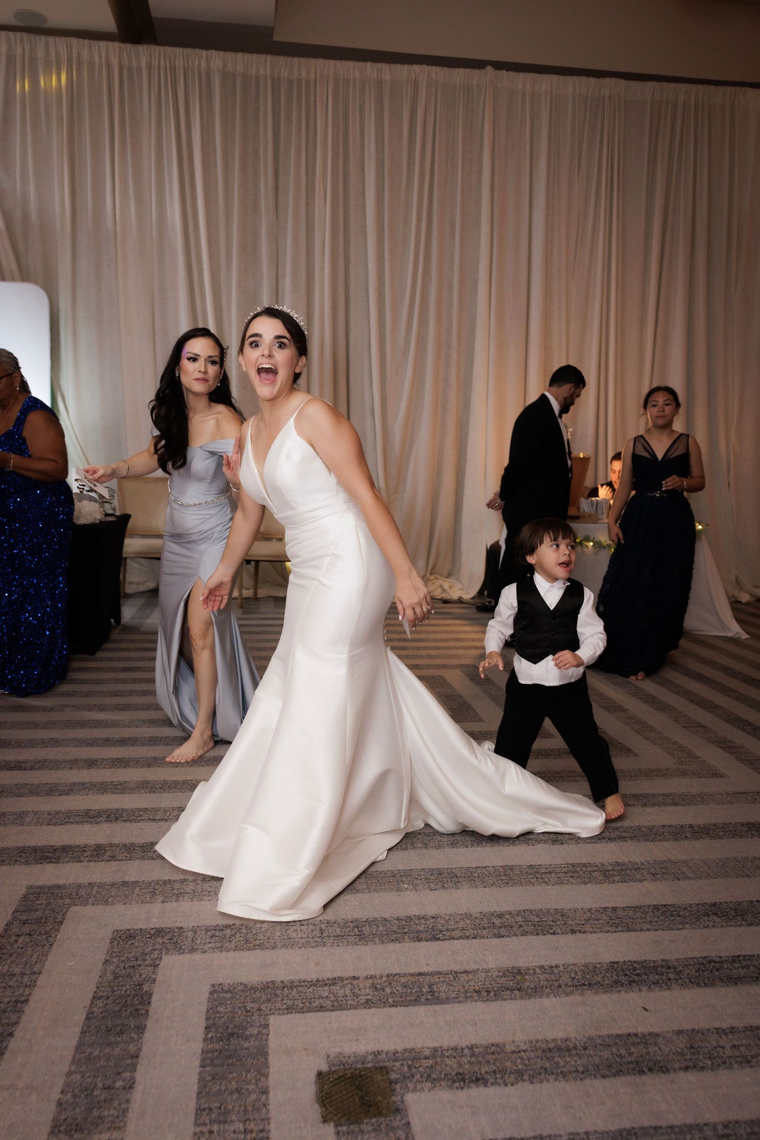 A sequence of wedding party guests dancing and moving across a patterned ballroom floor during a celebration.