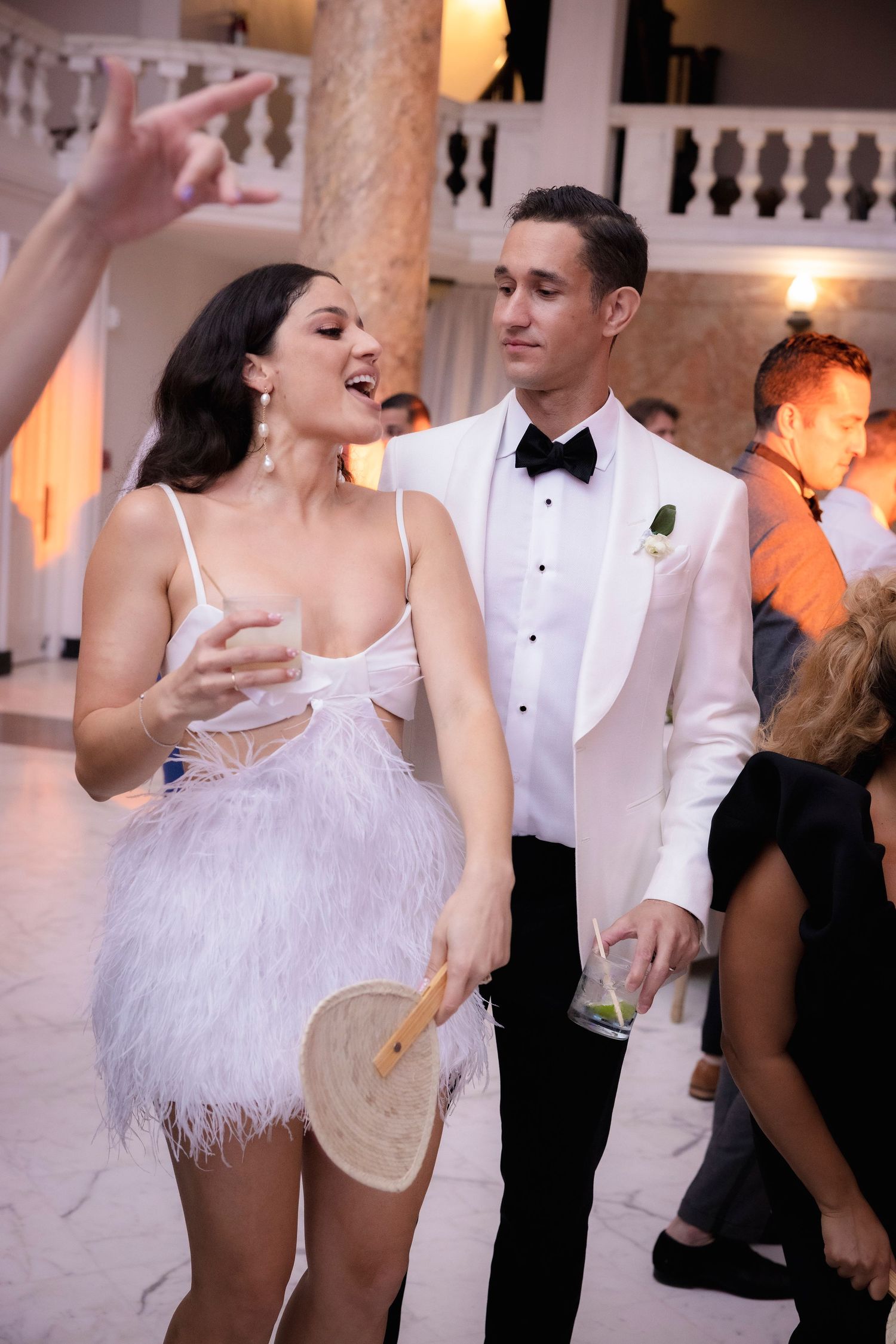 A couple dances joyfully at an elegant wedding reception with ornate decor visible in the background.