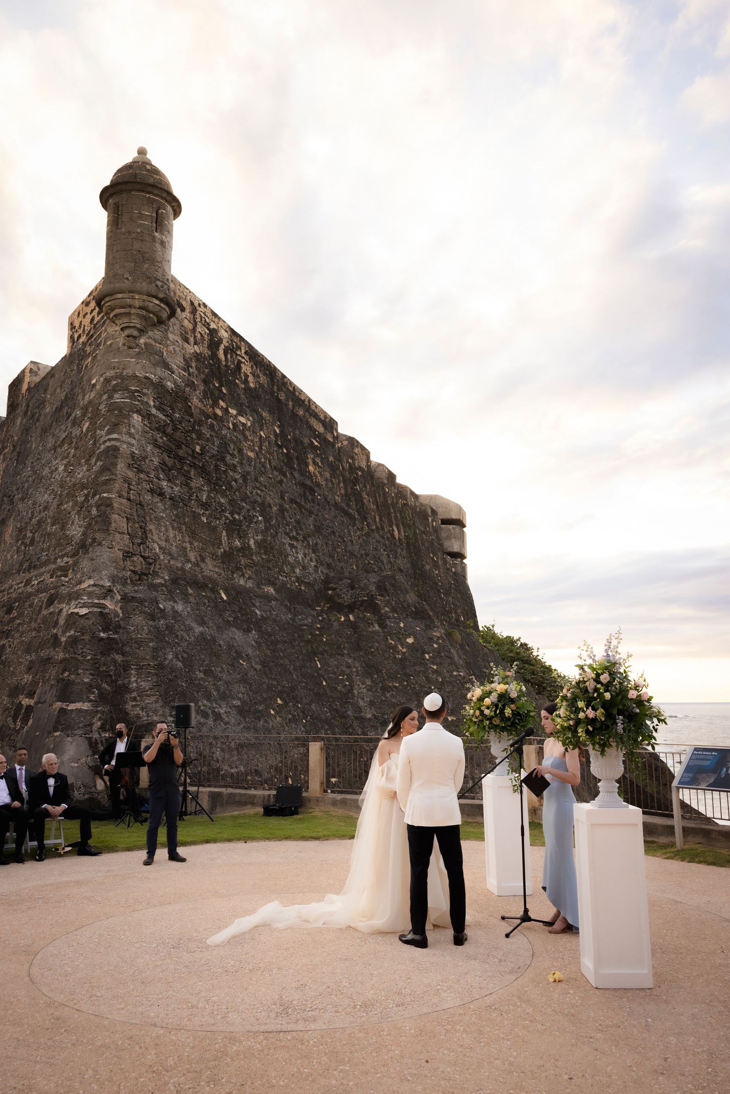 Wedding ceremony at a historic stone fortress overlooking a scenic landscape at sunset.