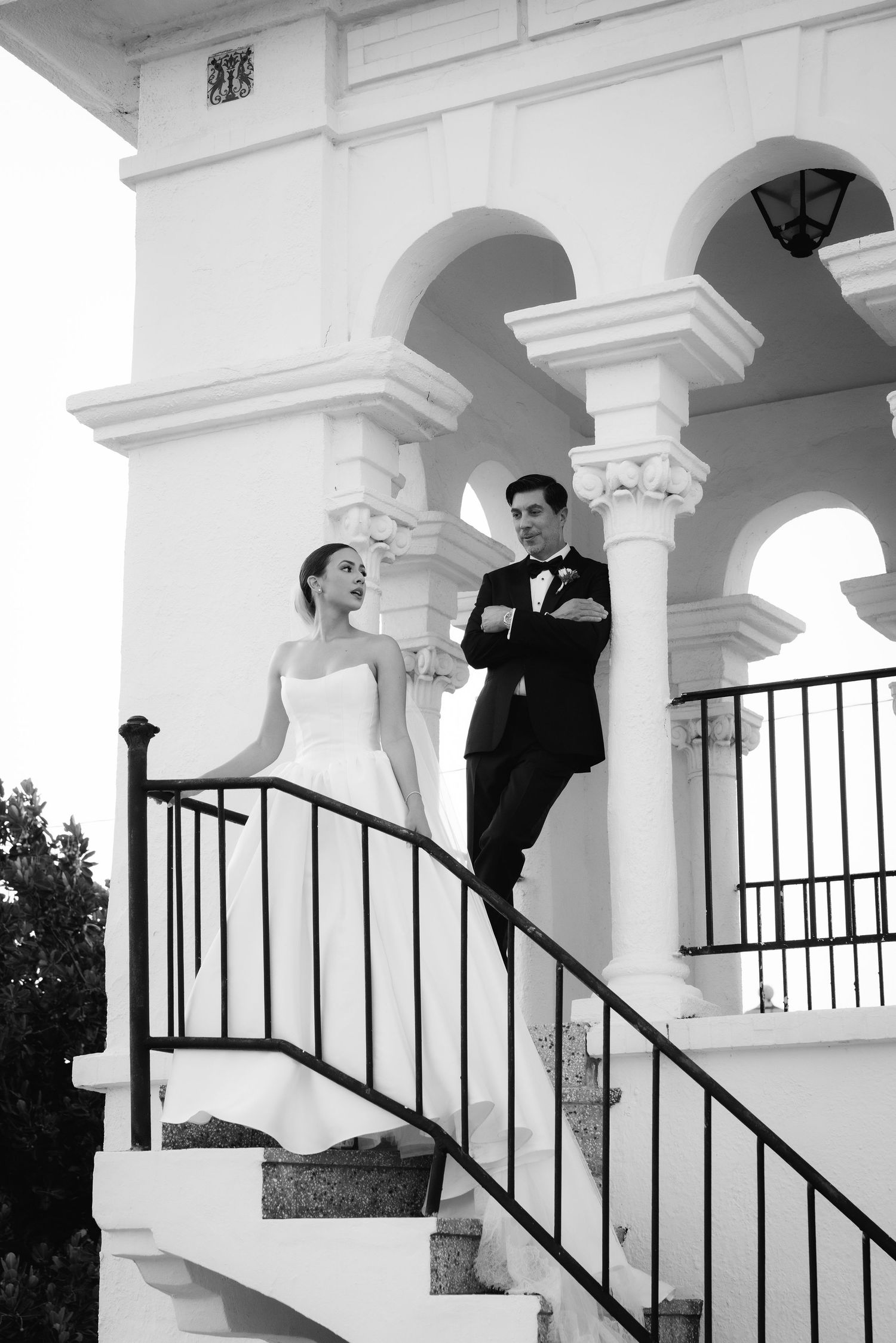 A romantic wedding couple poses under white archways and railings in a series of elegant black and white photos.