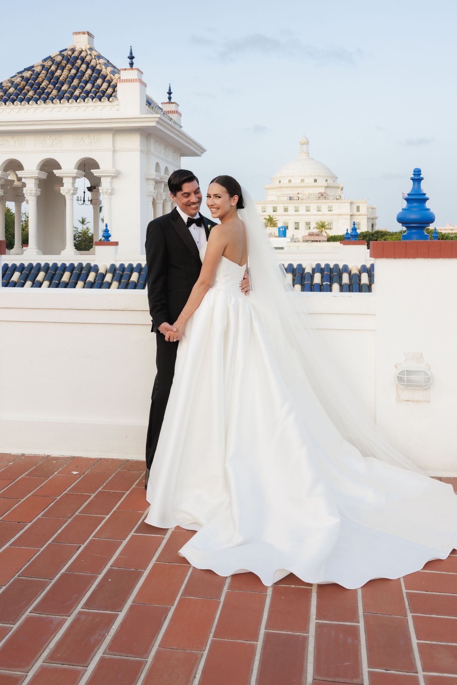 An elegant wedding portrait on a Spanish-style terrace with white domed architecture and blue accents.