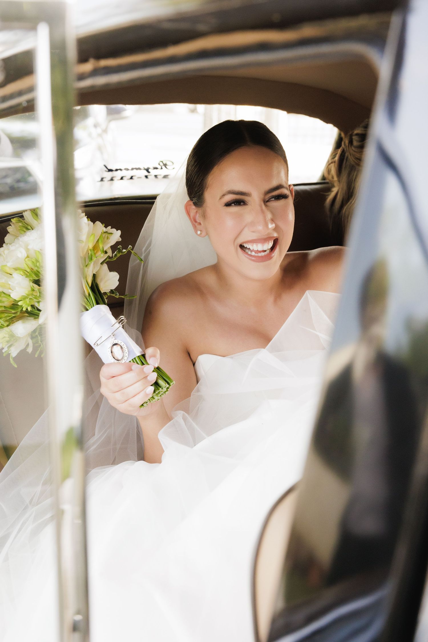 Joyful bride smiling in classic white wedding gown inside vintage car on her special day.