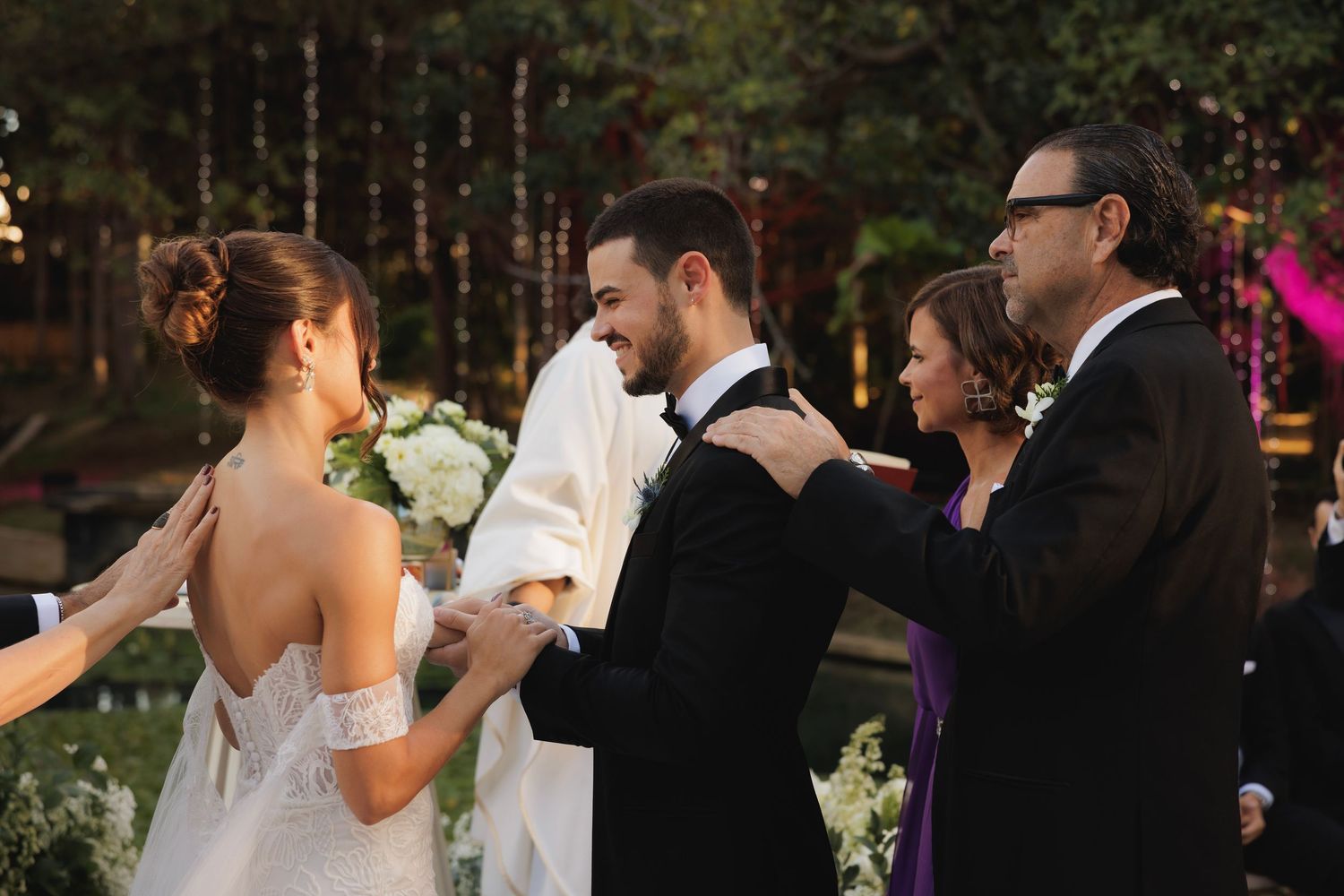 Wedding celebration at dusk with guests gathered around bistro chairs under twinkling lights.