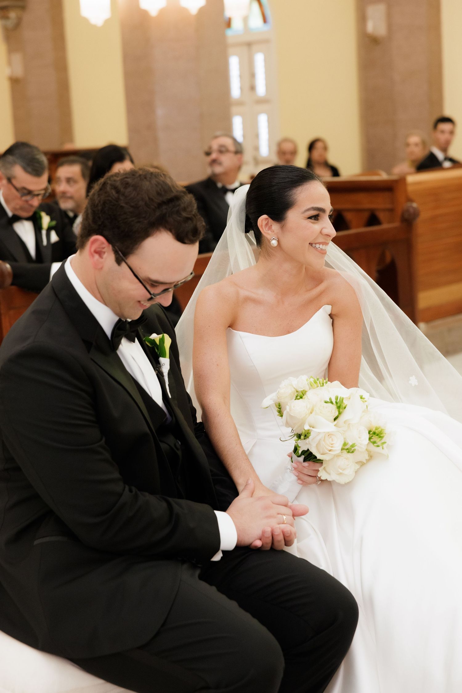 A candid moment during a church wedding ceremony with white floral bouquet details.