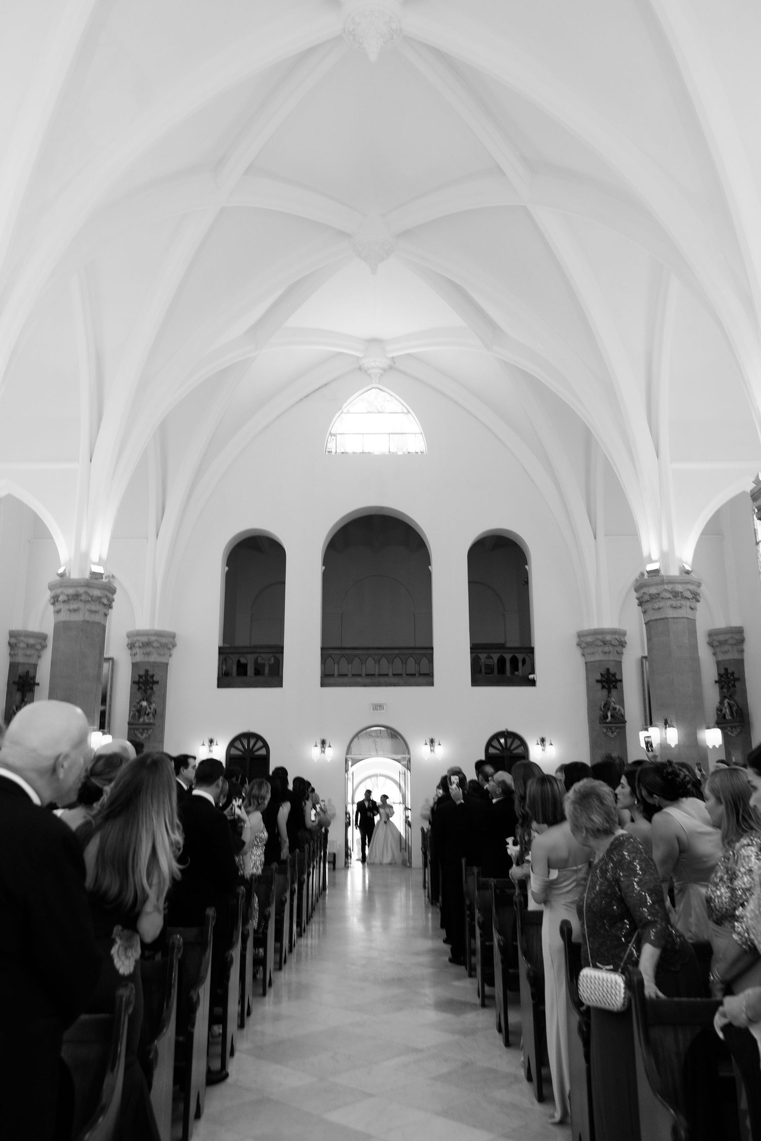 Wedding ceremony in gothic-style white church with vaulted ceilings and filled pews.
