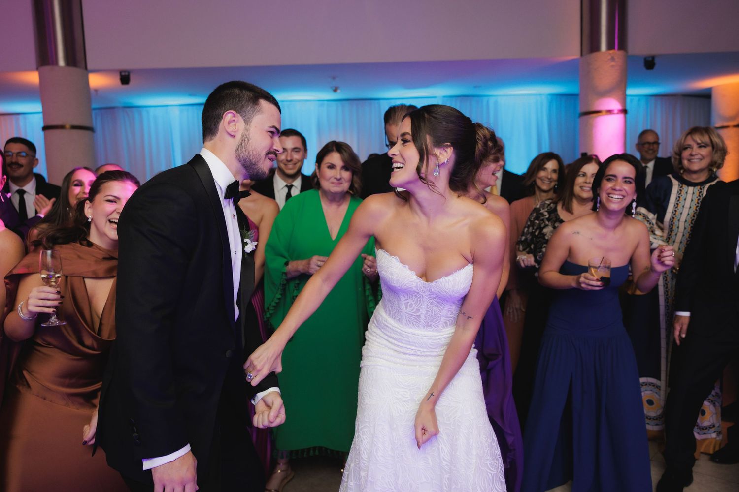 Wedding guests dance and celebrate on a vibrant dance floor illuminated with blue and purple lighting.