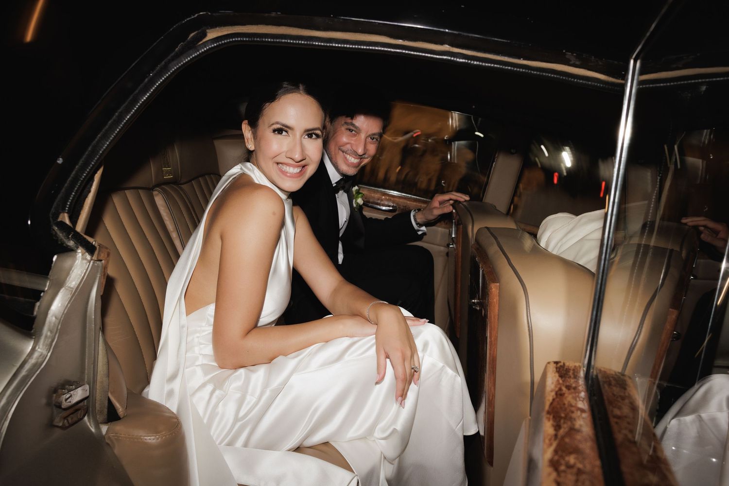 Newlyweds share a happy moment inside a vintage car with luxurious leather interior.