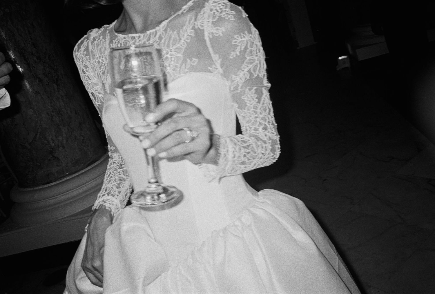 Bride in lace wedding gown holding a crystal champagne glass in a black and white photo.