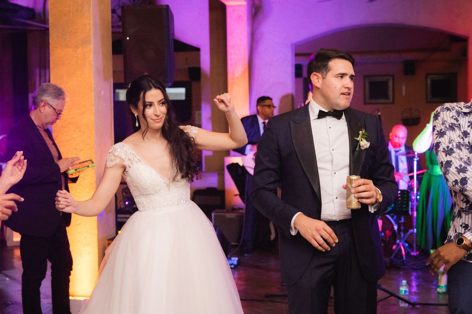 People dancing at a wedding reception with purple and orange uplighting in an elegant ballroom venue.