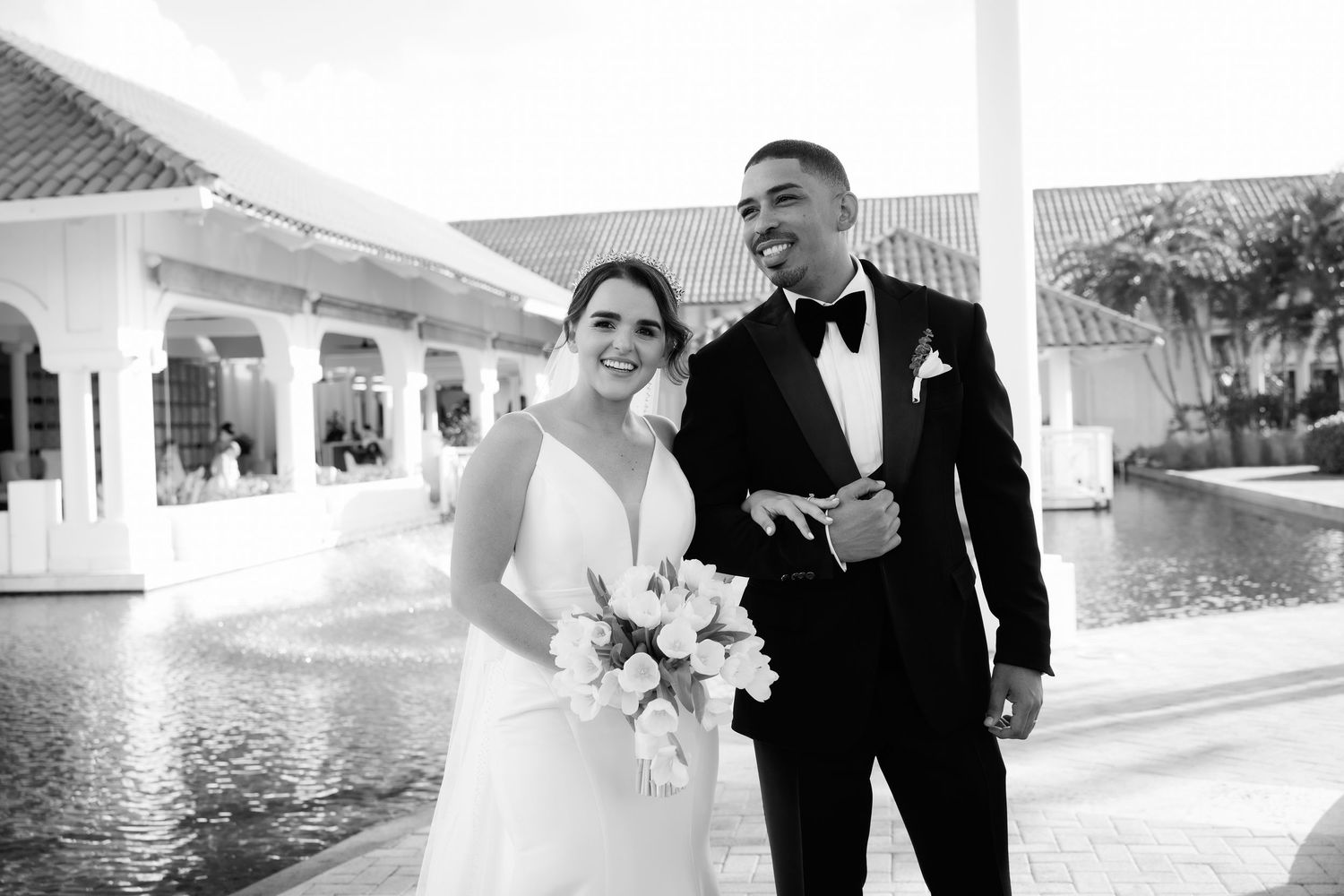 A couple walks and laughs together while dressed in formal wedding attire on their special day.
