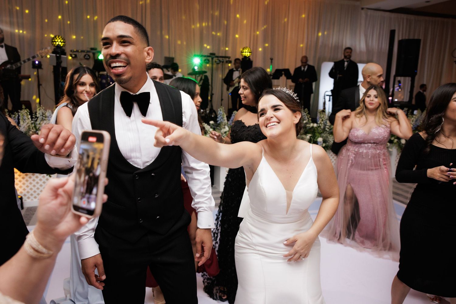 Guests celebrate with dancing and laughter at an elegant wedding reception with pink decor and twinkle lights.