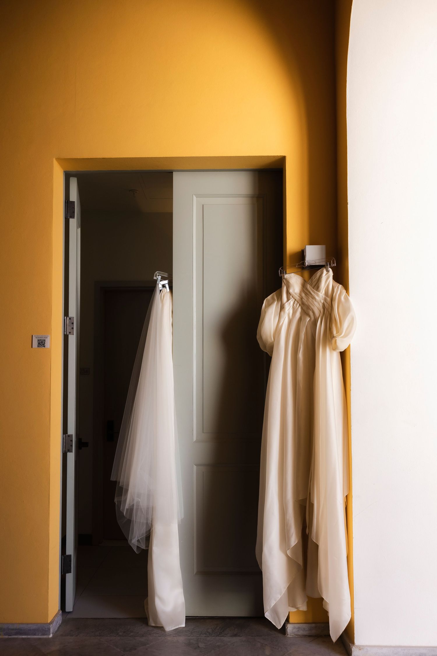 Wedding dress and veil hanging elegantly in a warmly lit hallway before the ceremony.