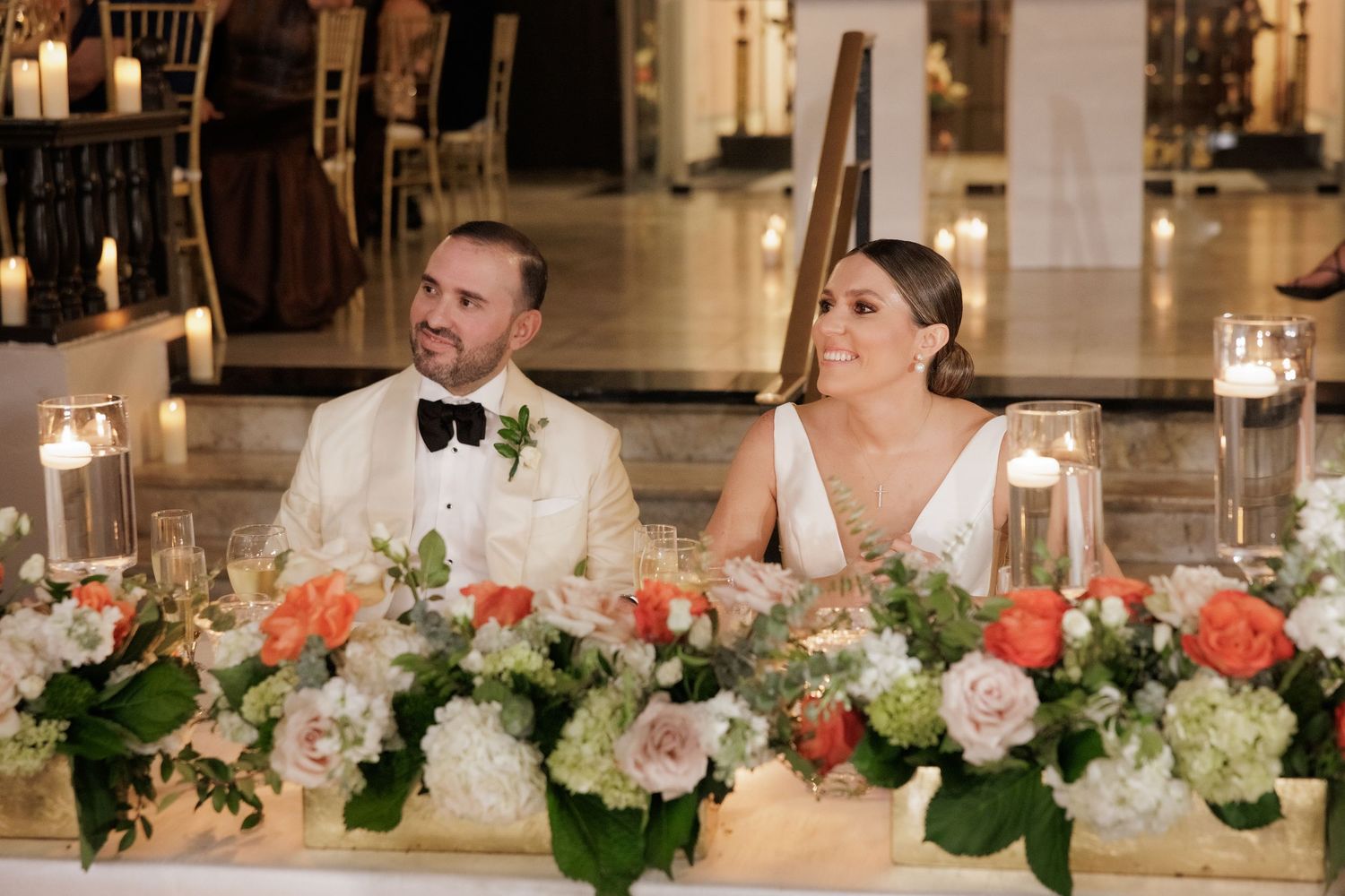 Elegant wedding reception table decorated with white and coral floral arrangements and glowing candles.