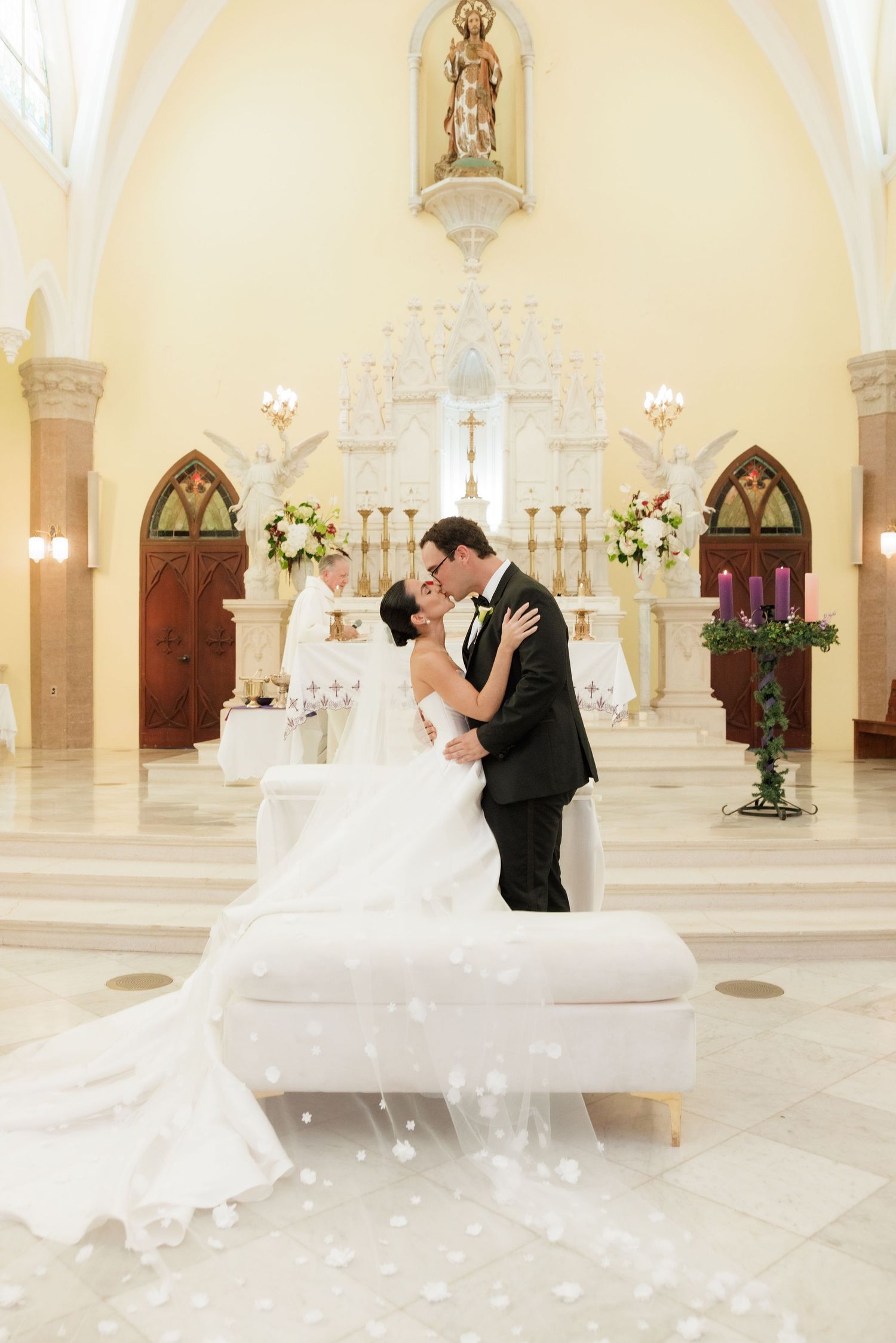 Elegant wedding couple dancing in a grand cathedral with ornate architecture and floral arrangements.