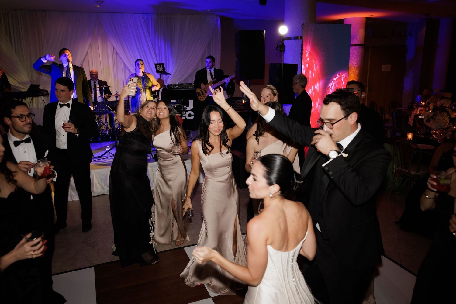 Energetic wedding reception dance party with guests raising their hands in celebration.