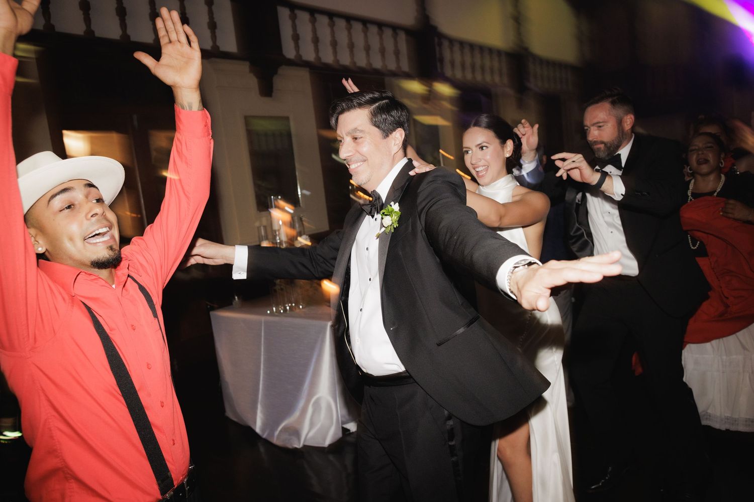 Wedding guests dancing and celebrating on a lively reception dance floor with red lighting.