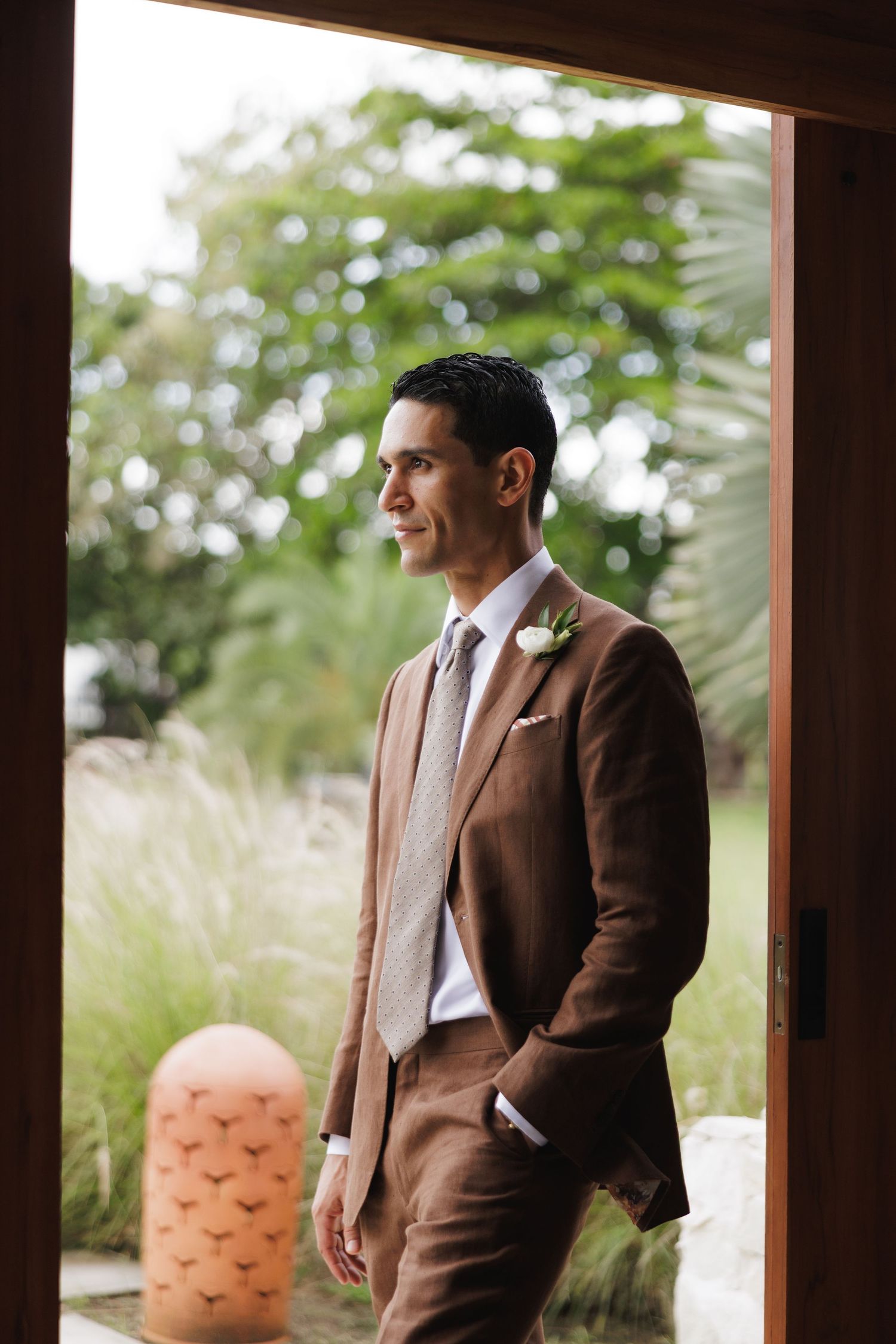 A formal portrait in a brown suit framed by tropical foliage and natural light.