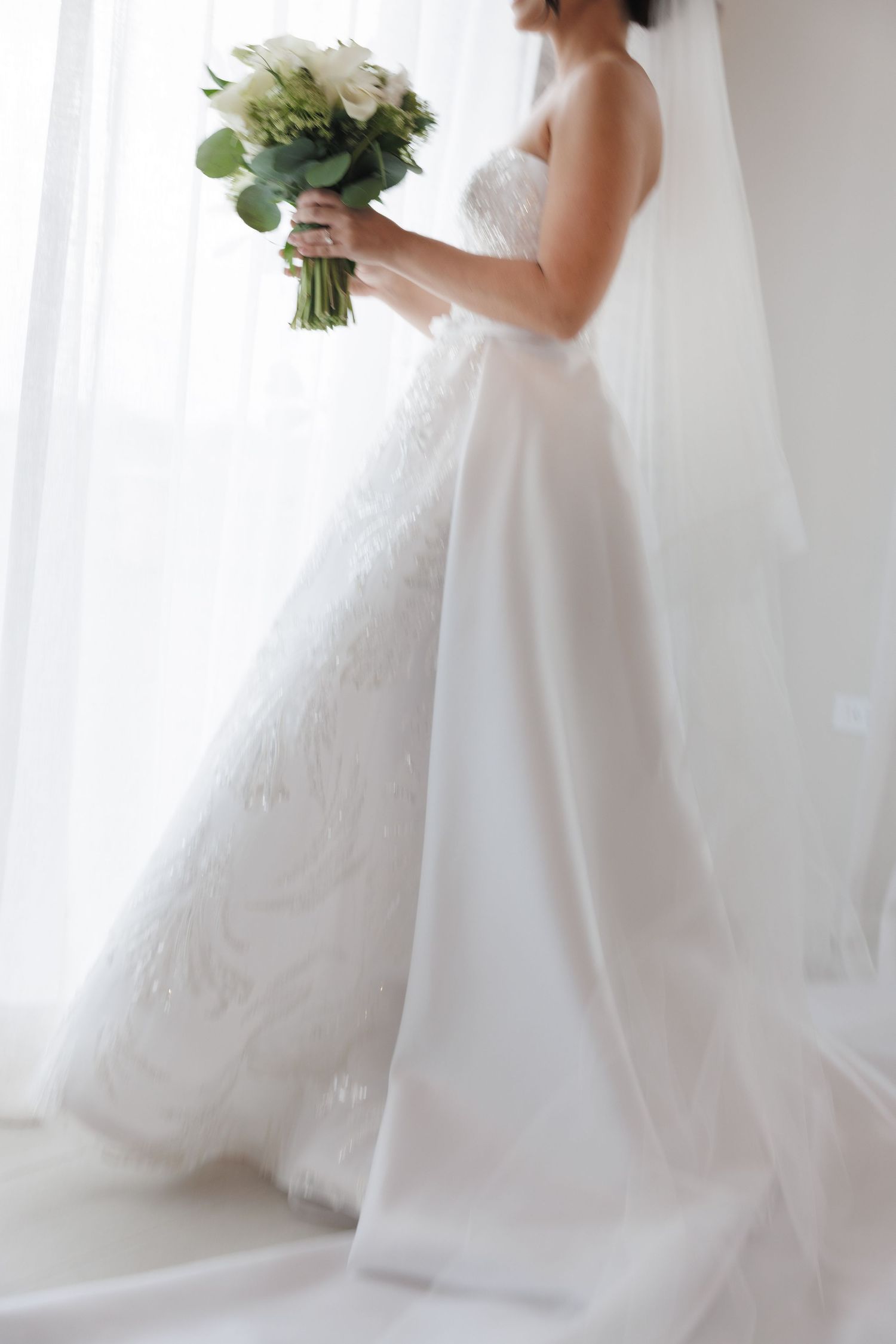 Elegant wedding dress details captured in soft natural light with white floral bouquet.
