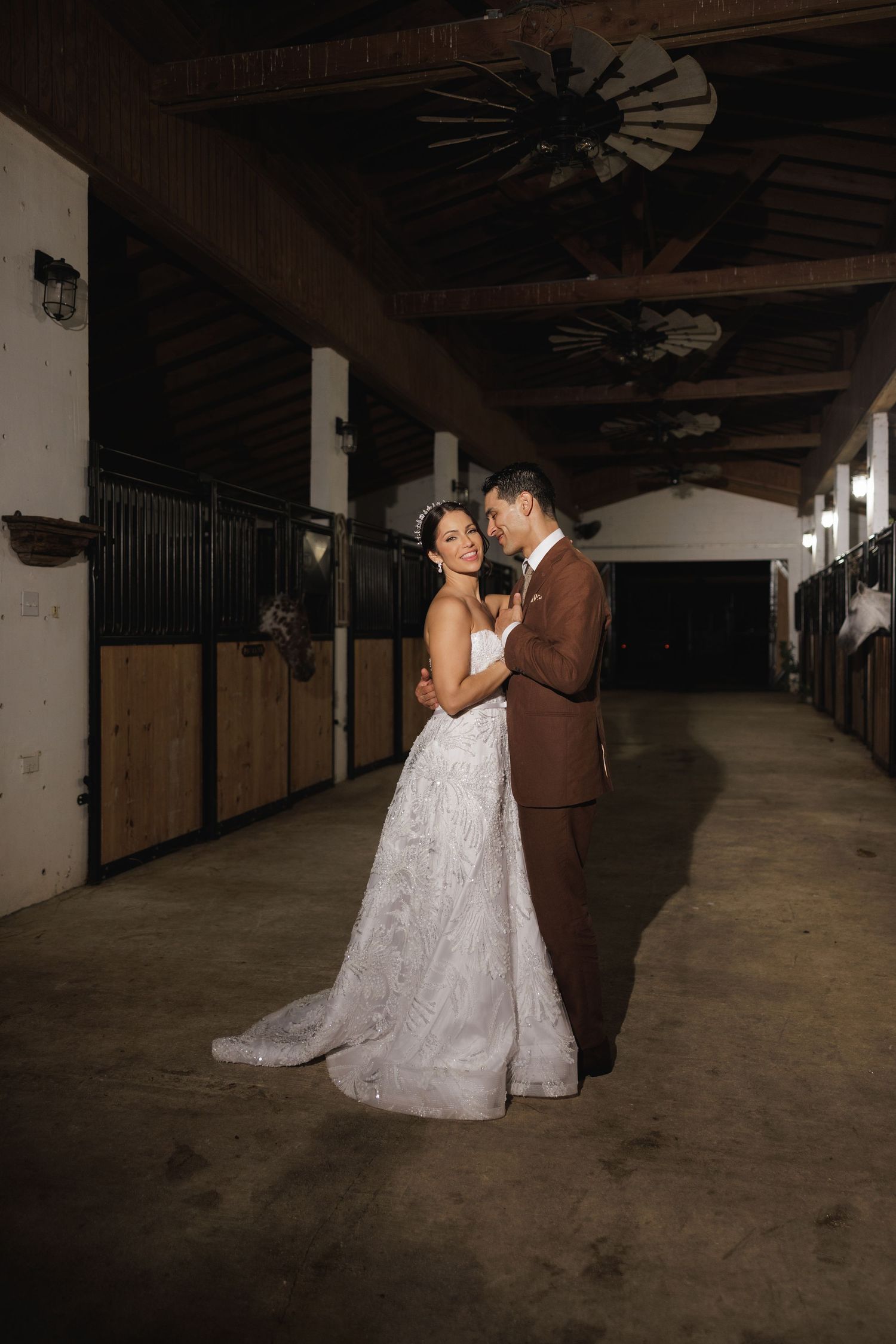 Bride and groom share romantic moments in a rustic barn stable with dramatic lighting.