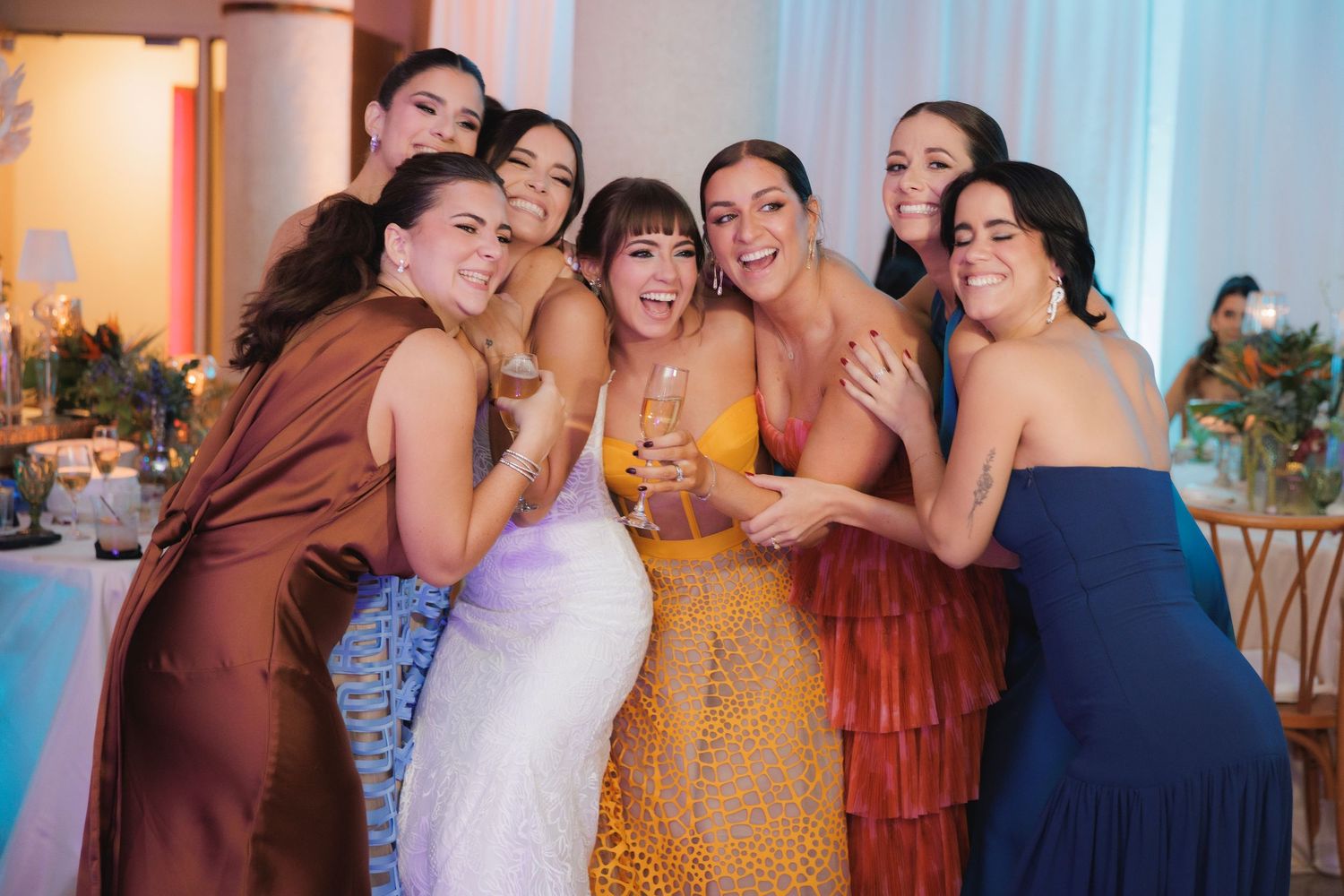 Wedding party members in colorful dresses celebrate together during a festive reception moment.