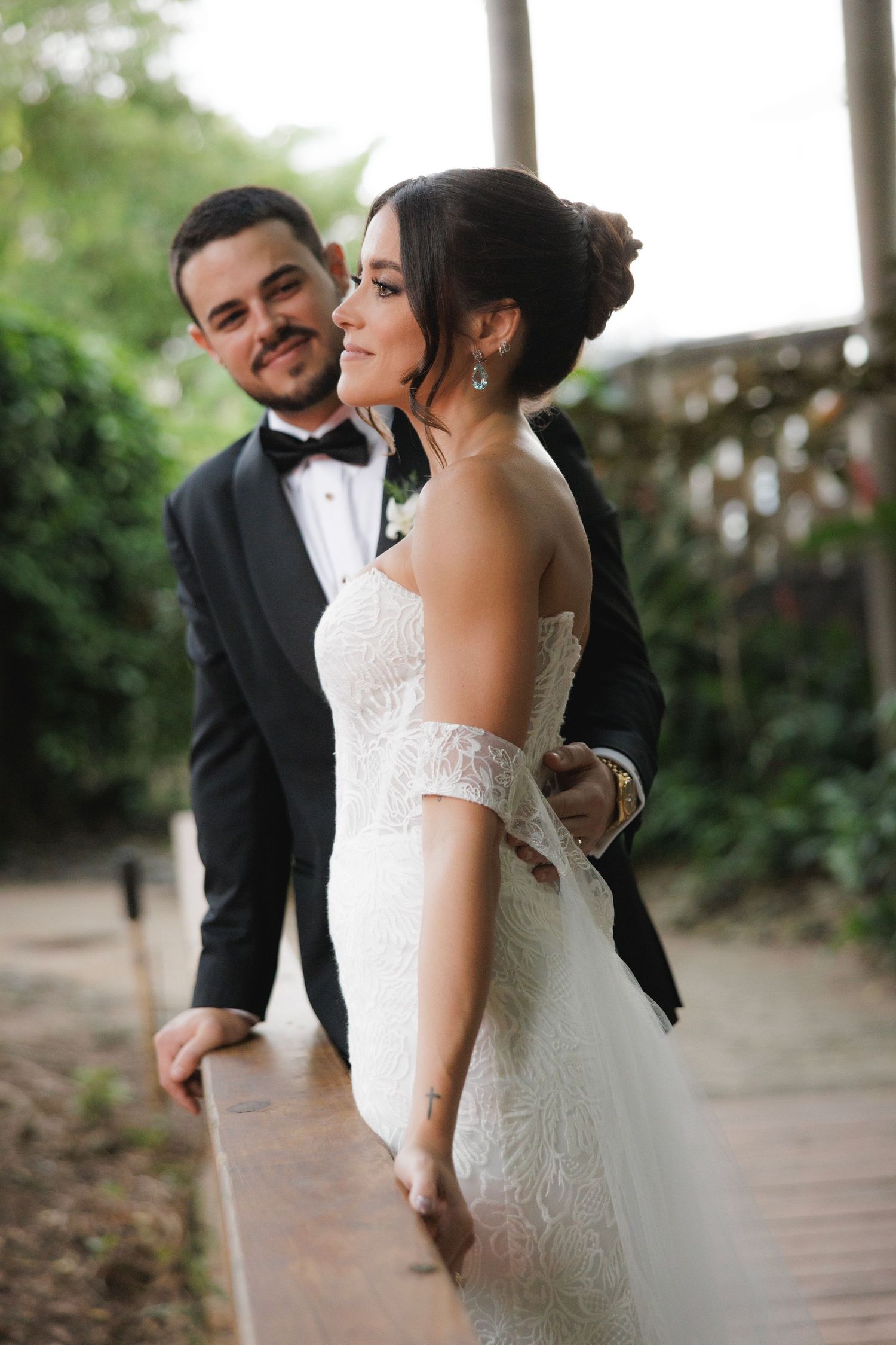 Newlyweds share playful moment on covered porch with bride in lace gown and groom in classic tuxedo.