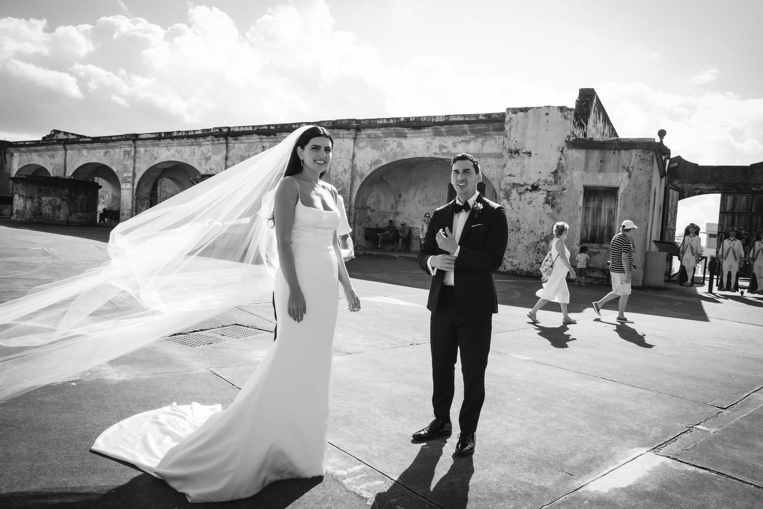 Wedding couple photographed in black and white with flowing veil creating dramatic movement across frames.