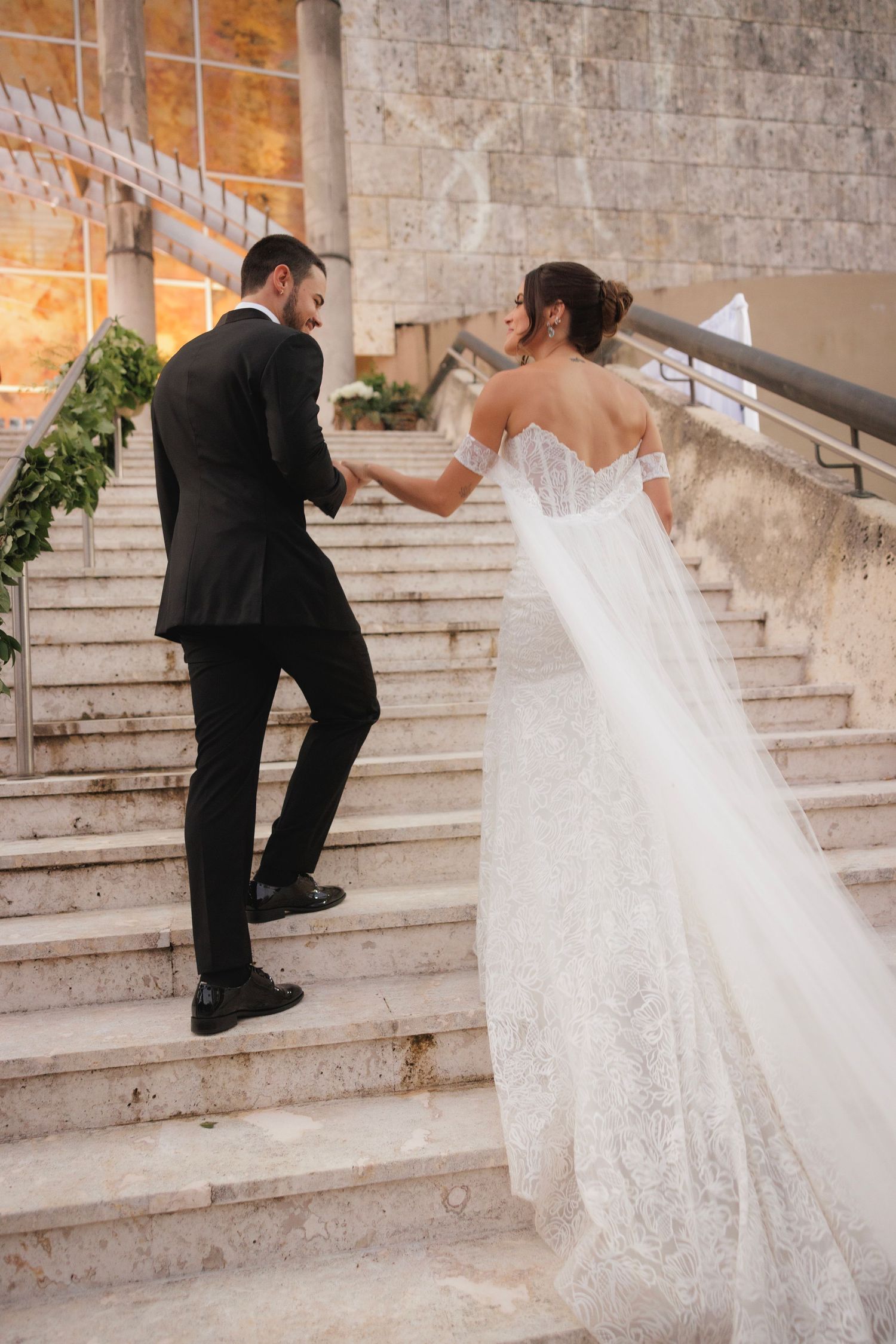 Wedding couple ascending stone stairs with bride holding her dress and groom leading the way.