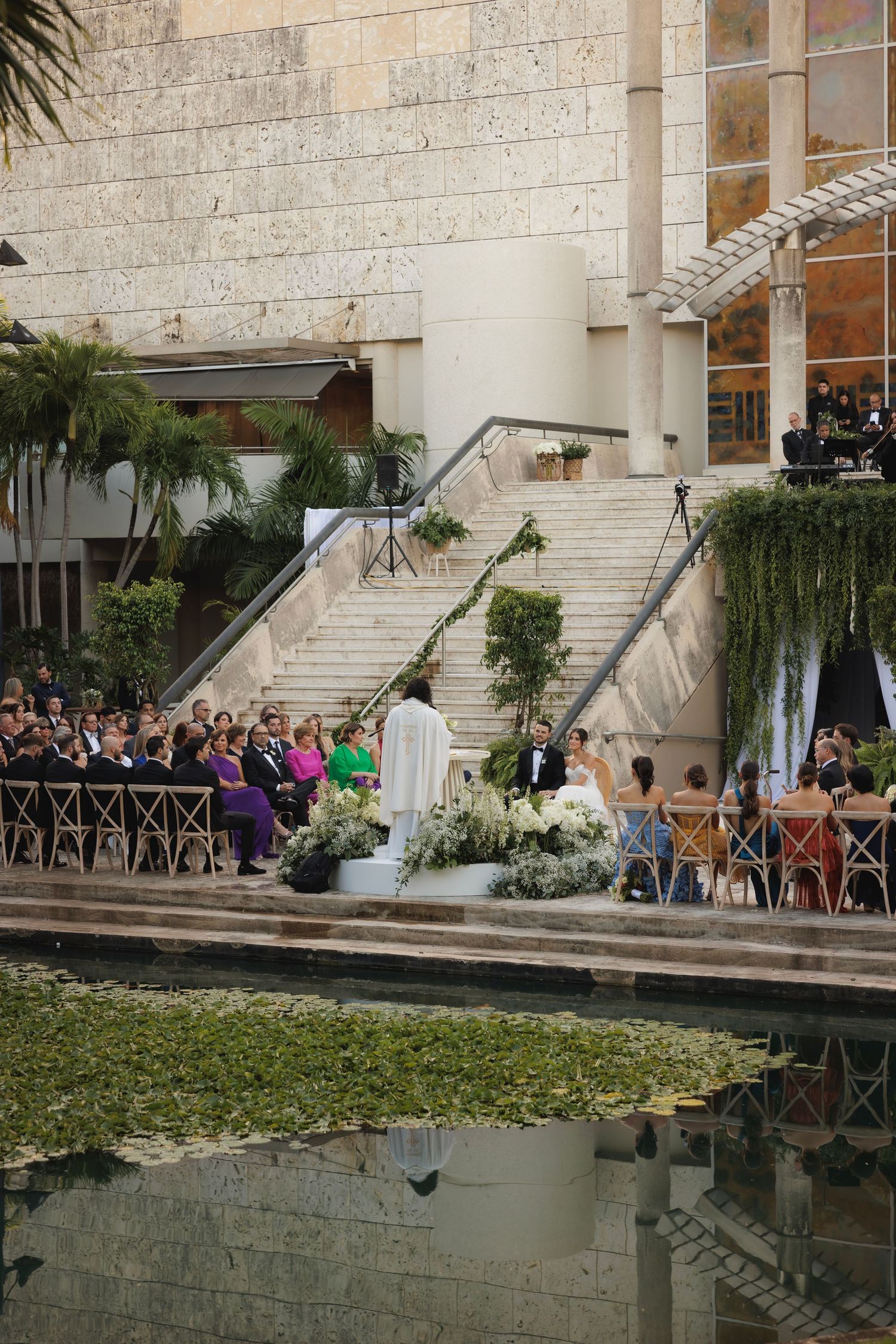 An outdoor wedding ceremony setup with white chairs and stairs leading to a reflecting pool at a modern venue.