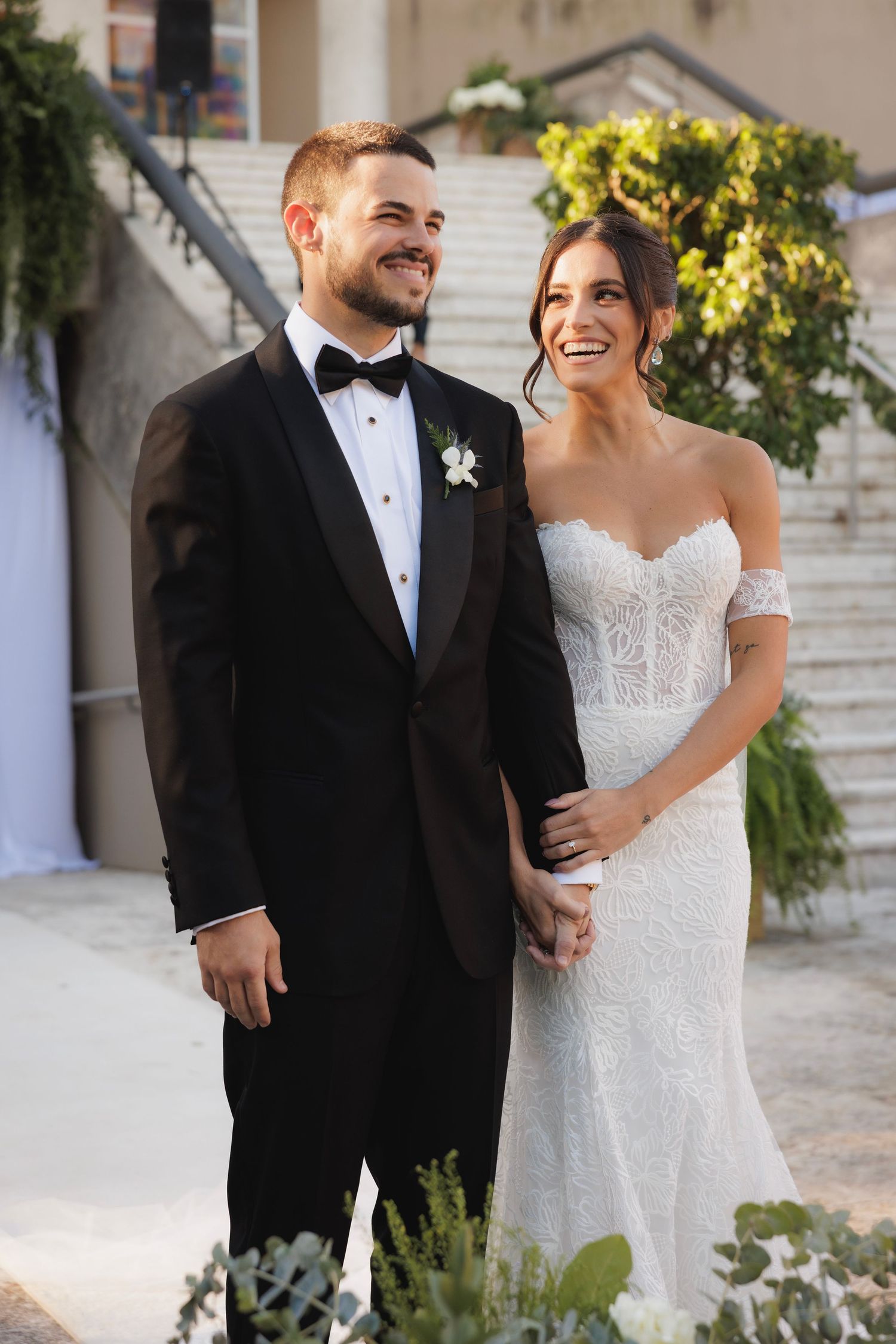 Wedding couple shares candid moments outdoors at a luxury venue with stone walls and natural lighting.