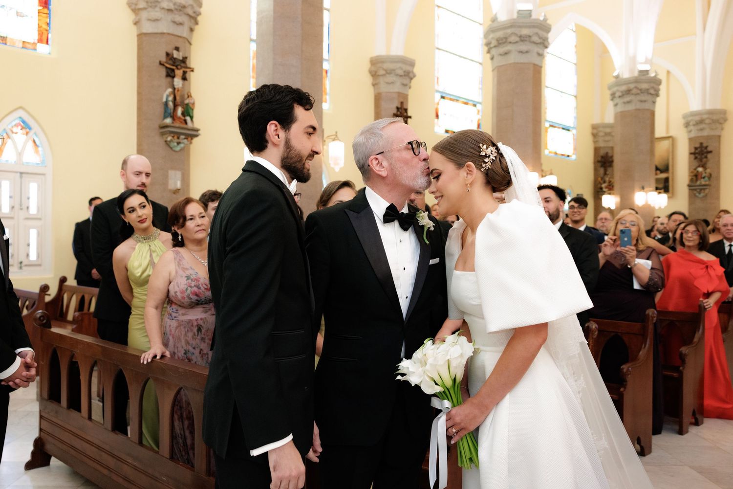Wedding ceremony in a grand church with couples exchanging vows while guests look on from traditional wooden pews.