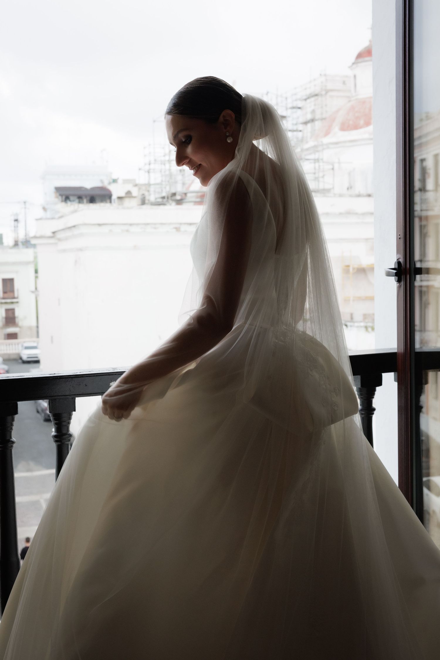 Silhouetted figure in a flowing white wedding gown stands against bright windows creating a dramatic backlit effect.
