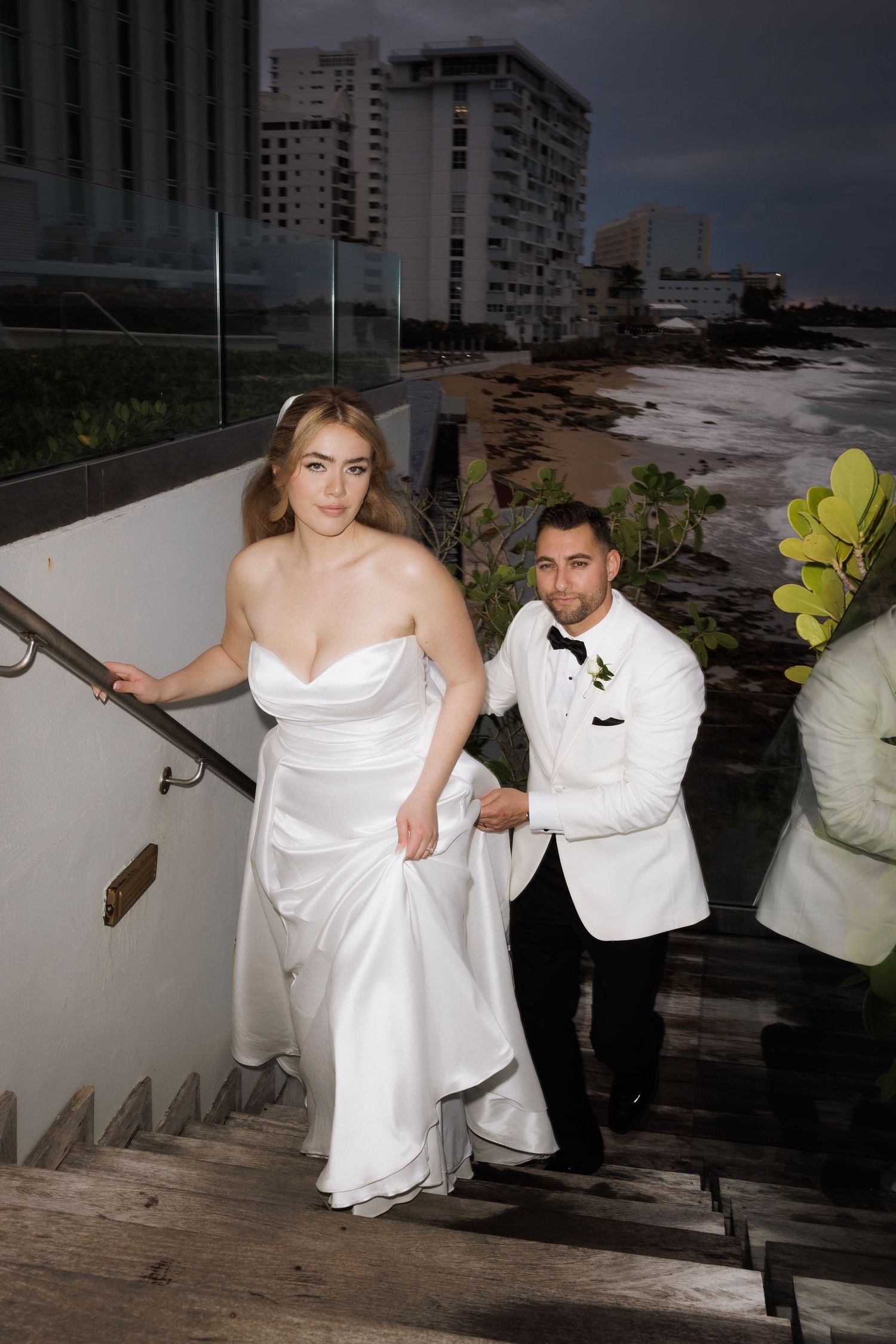 Wedding party ascending outdoor stairs with bride in white dress and attendants in formal attire.
