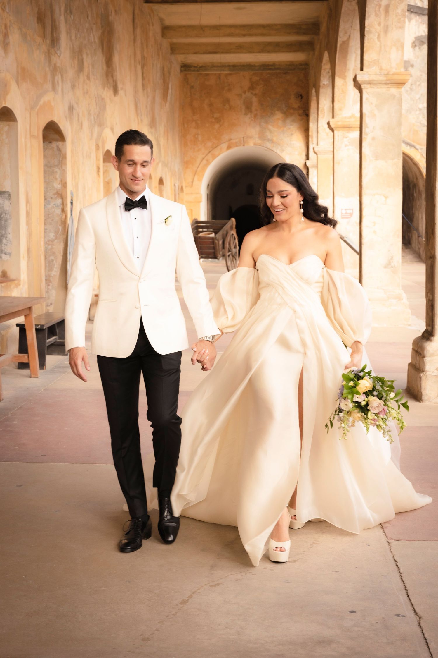 Wedding couple walking through stone colonnade with beautiful natural lighting.