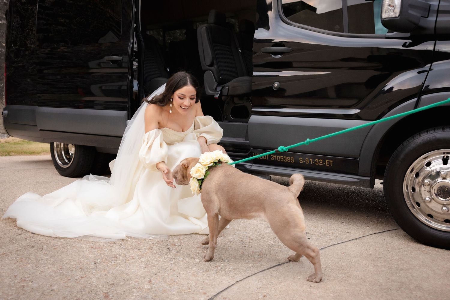 Playful moments between newlyweds and their dog near a parked vehicle after wedding ceremony.