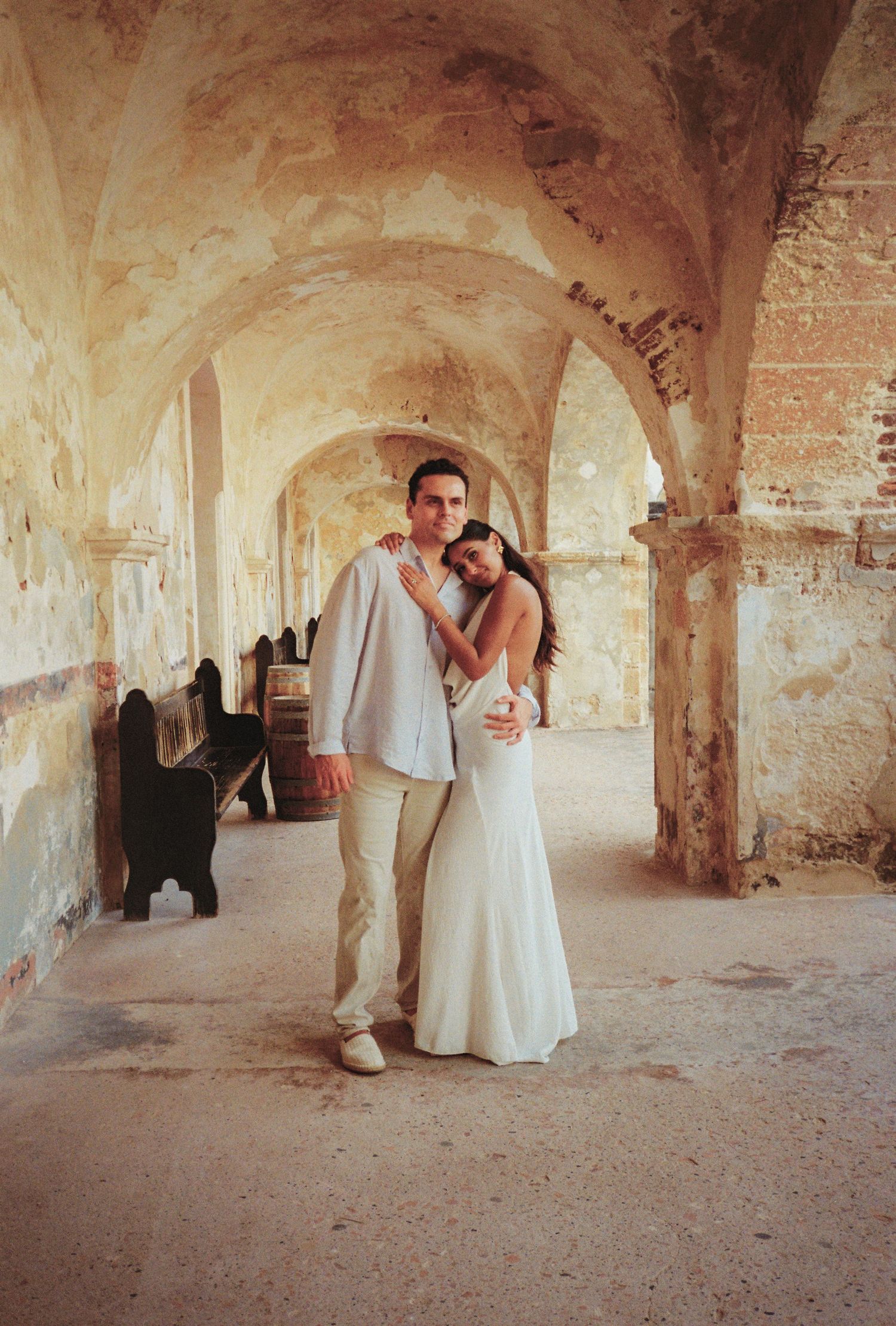 Elegant couple in wedding attire embracing in a rustic arched stone corridor with vintage charm.