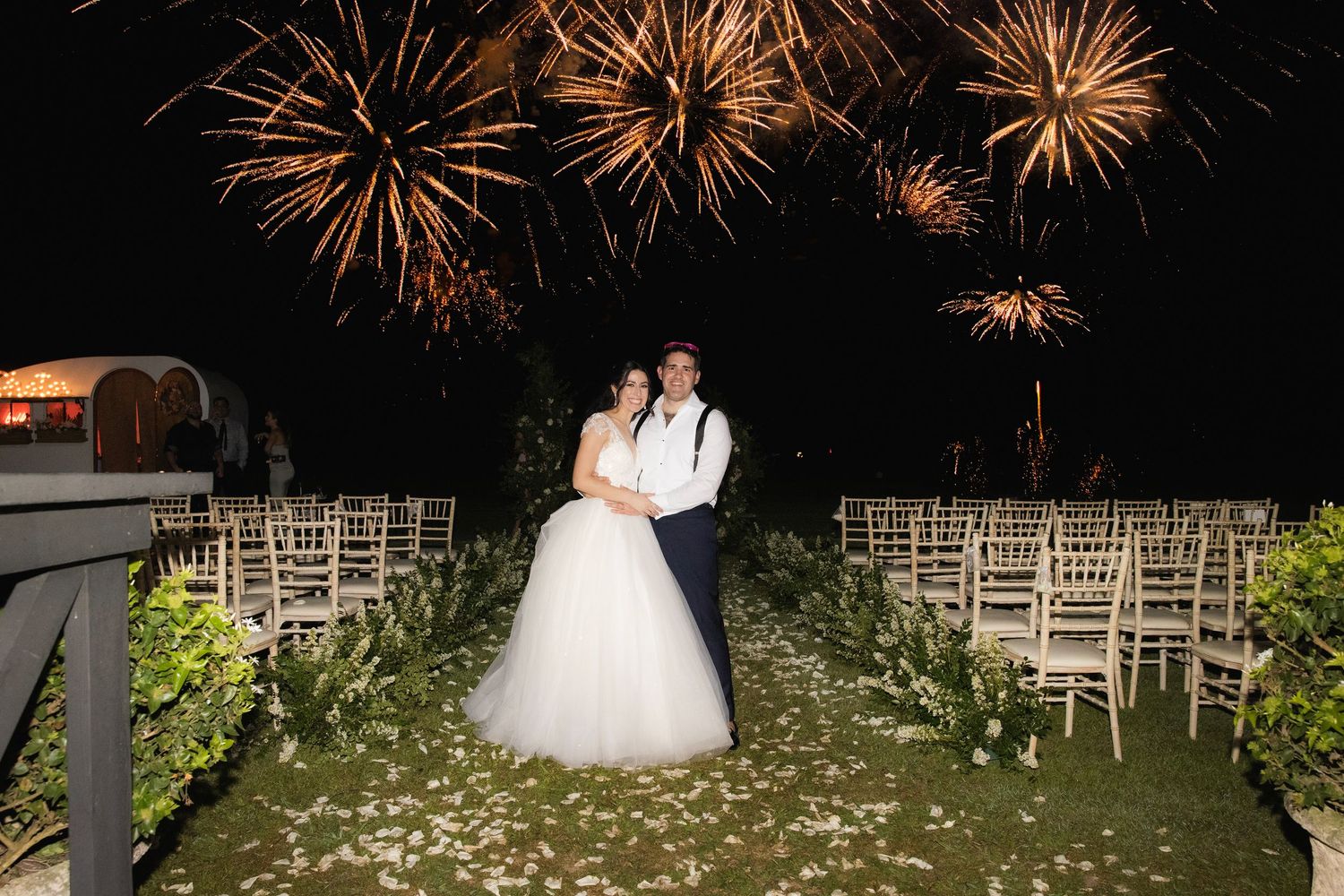 Fireworks light up the night sky over a wedding ceremony setup with white chairs arranged in rows.