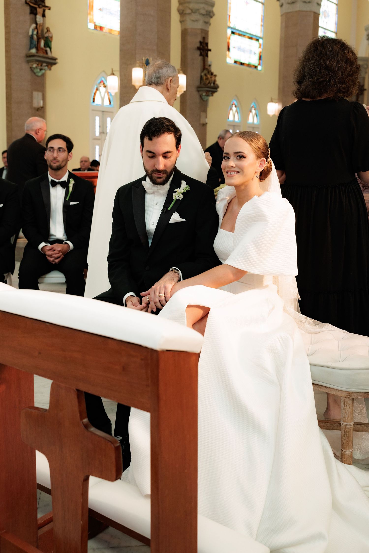 A couple shares a joyful moment during their wedding ceremony inside an ornate cathedral with stained glass windows.