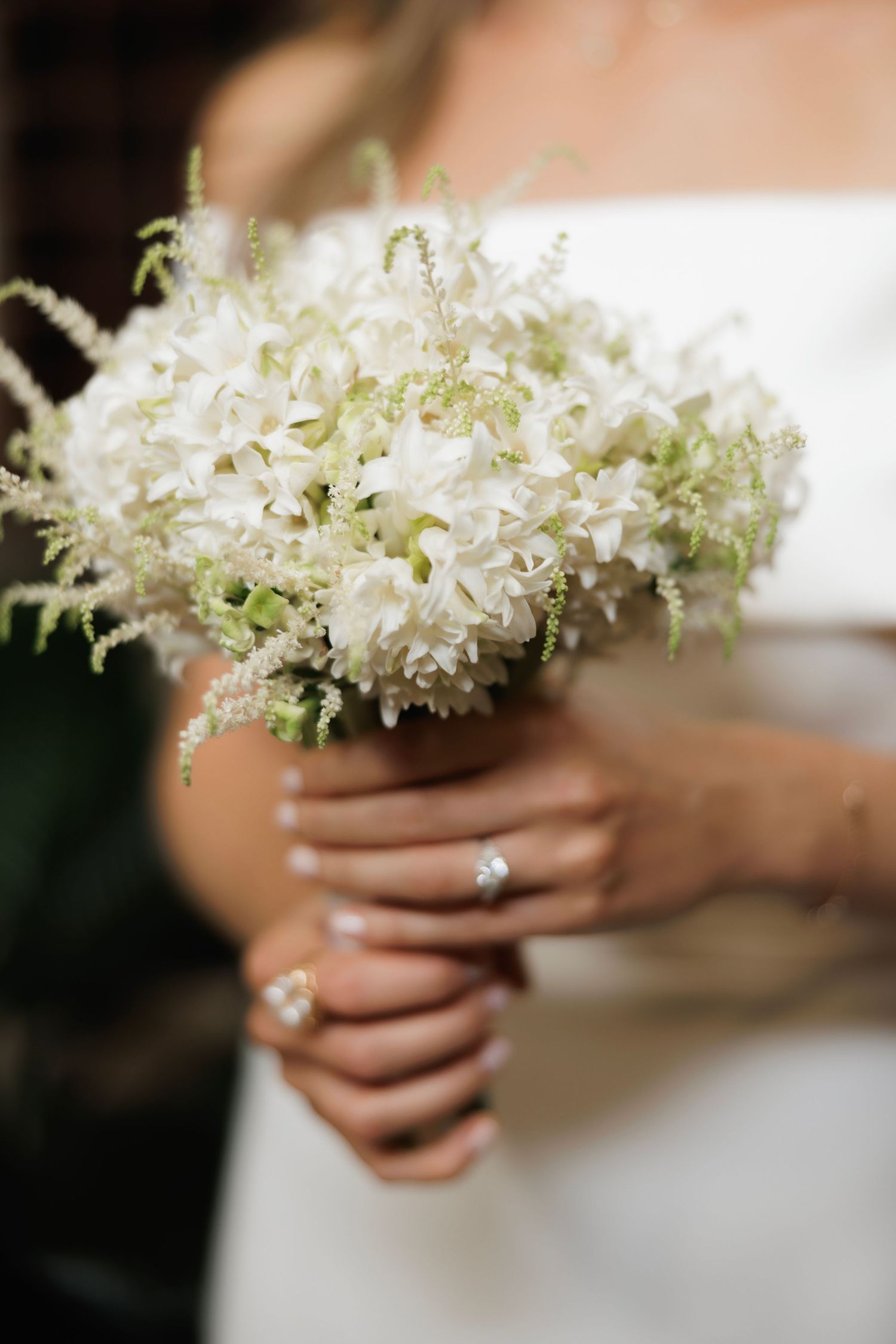 A delicate white bridal bouquet with small clustered flowers is held by hands wearing a sparkling engagement ring.