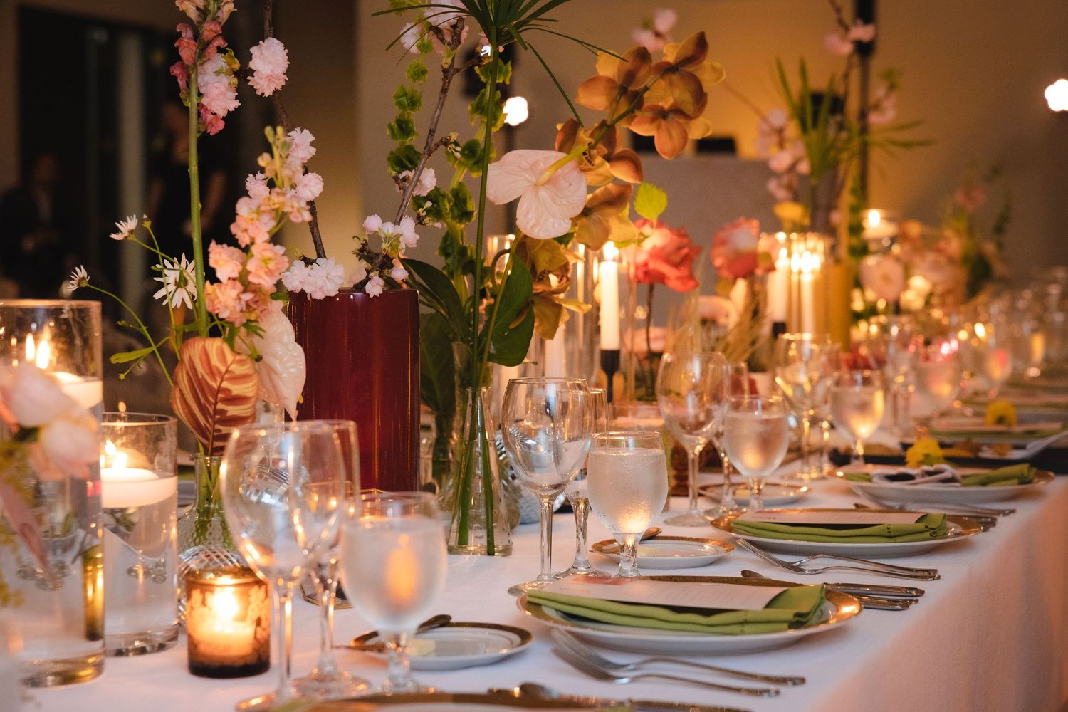 Candlelit wedding reception tables with elegant place settings, florals and glowing ambient lighting create a romantic atmosphere.