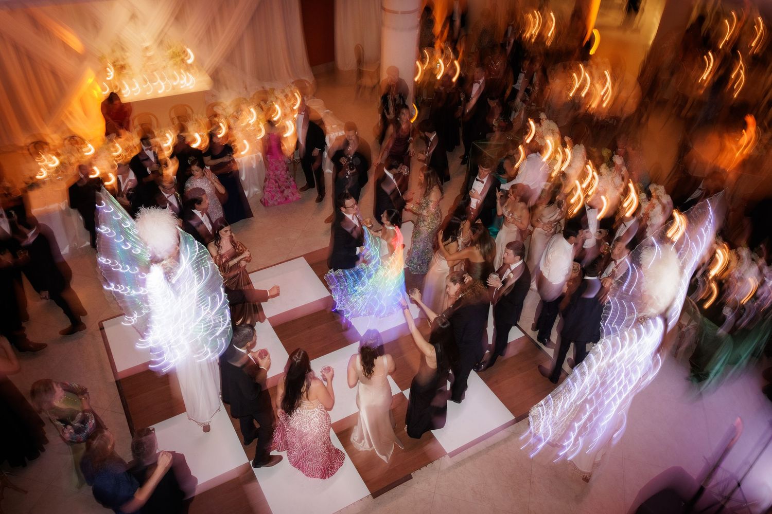 Wedding reception guests dancing on a ballroom floor with warm lighting and motion blur creating a dreamy atmosphere.