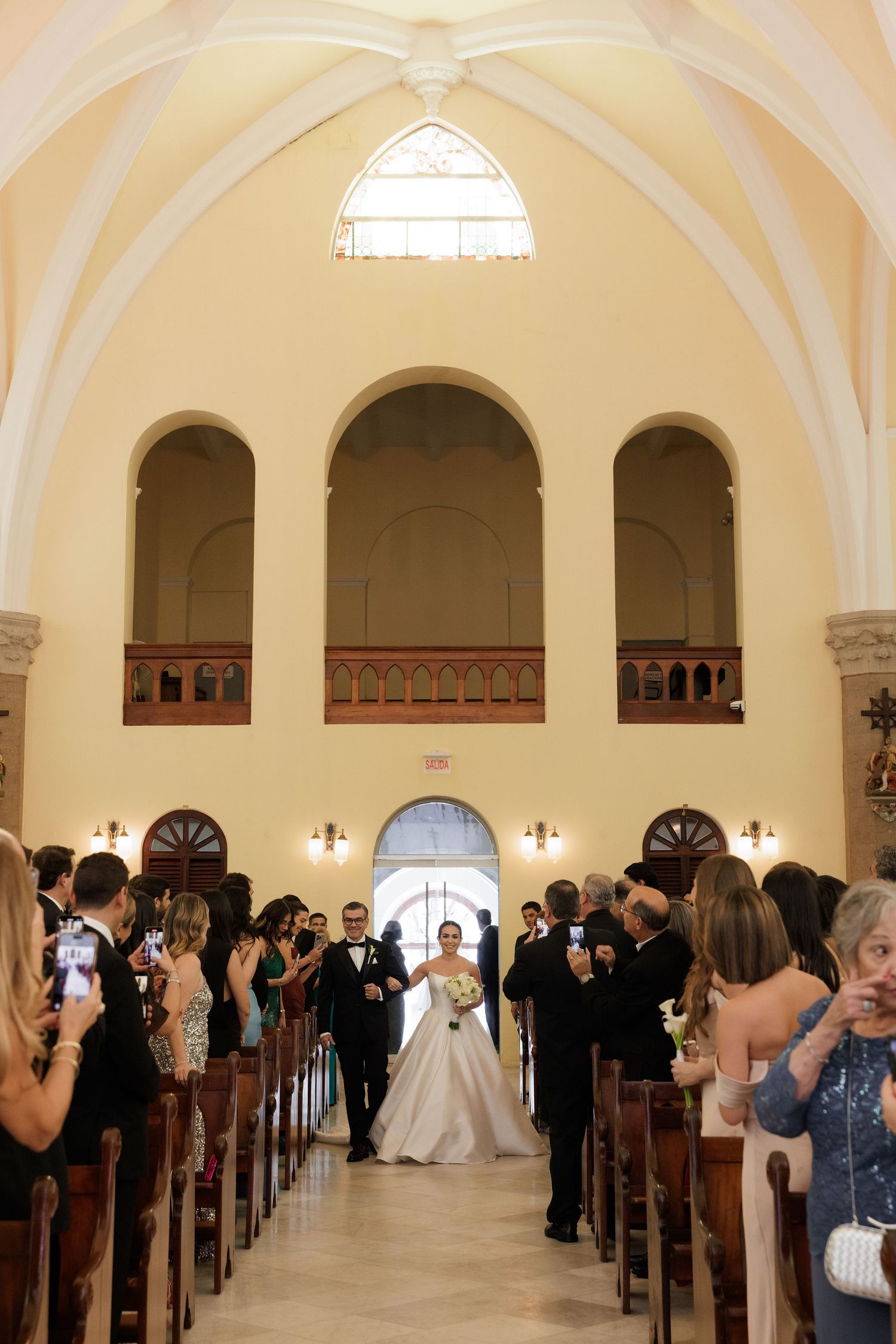 Wedding ceremony in a beautiful church with vaulted ceilings and guests lining the pews.