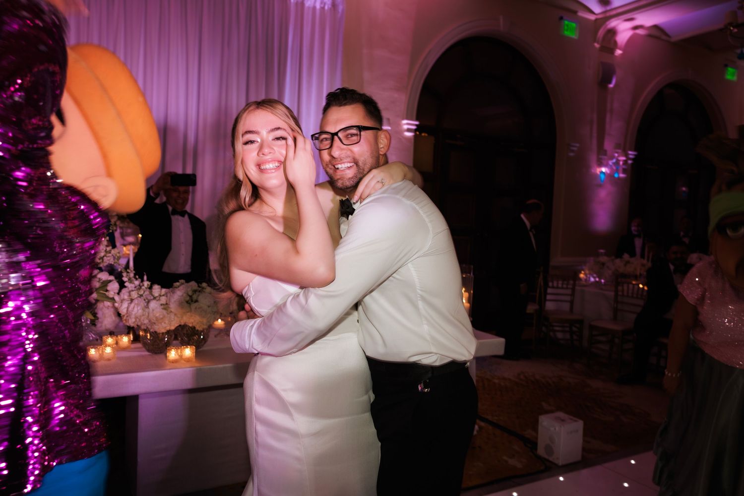 Wedding reception dance floor filled with guests enjoying the celebration under purple mood lighting.