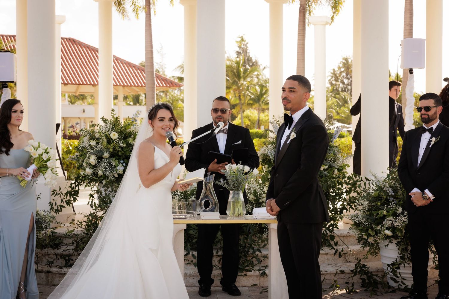 Wedding party gathered on an elegant white columned porch during sunset ceremony at outdoor venue.